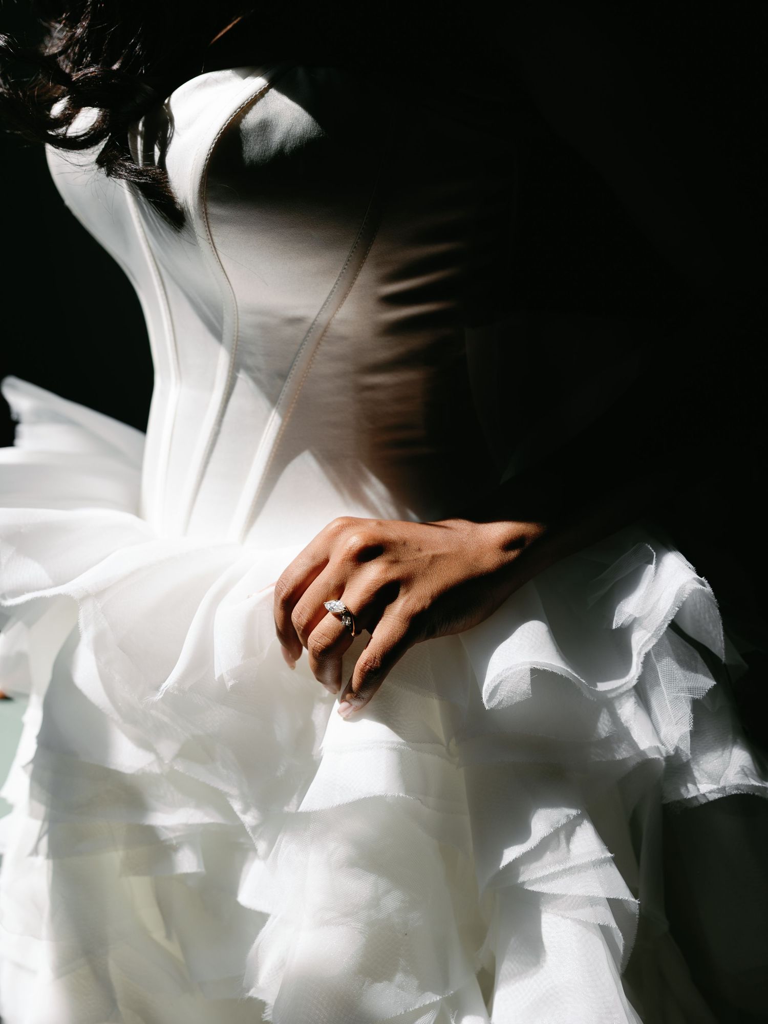 Close-up of bride's hand with diamond engagement ring on dramatic white ruffled wedding gown.