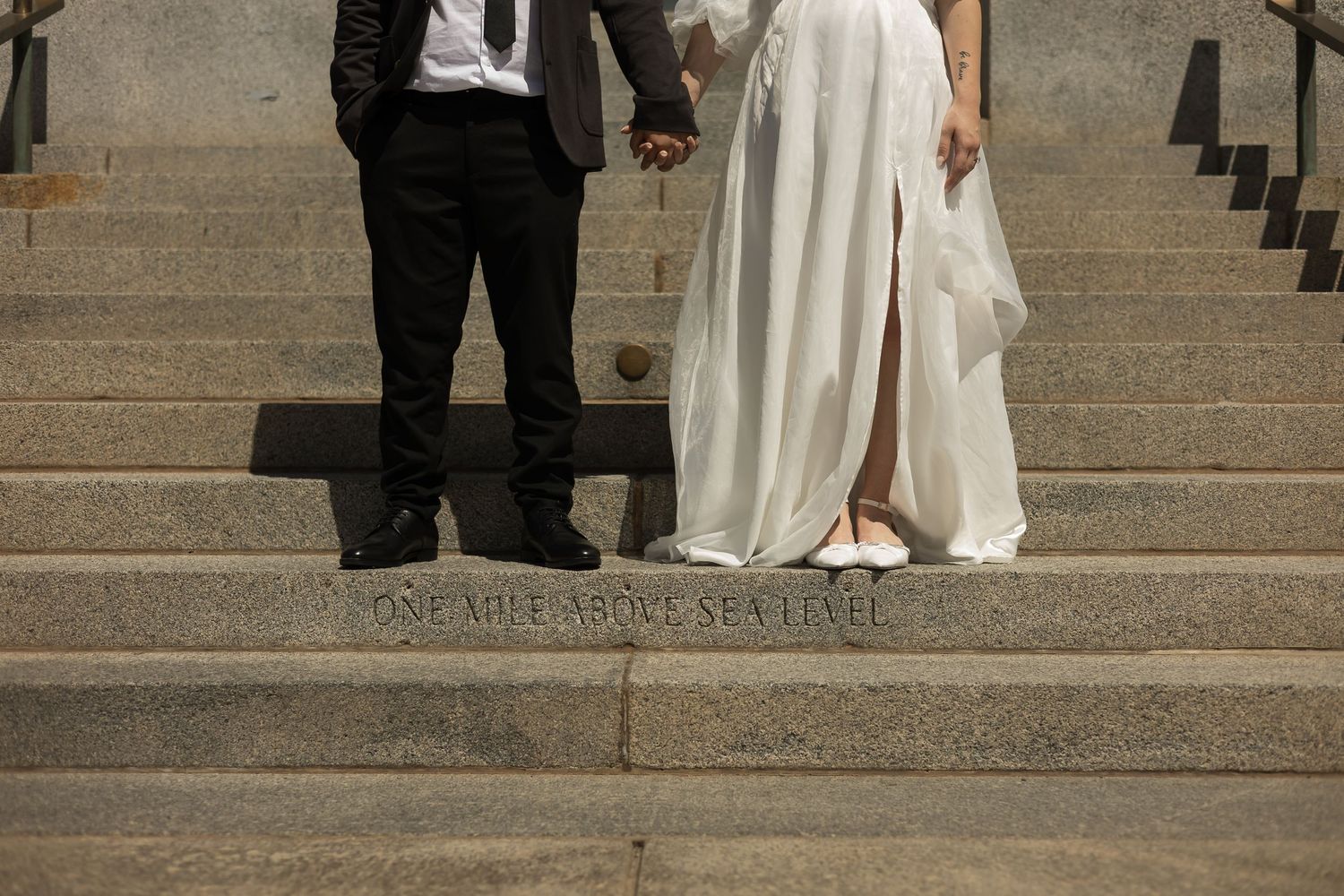 Wedding couple posing on stone steps in formal attire.