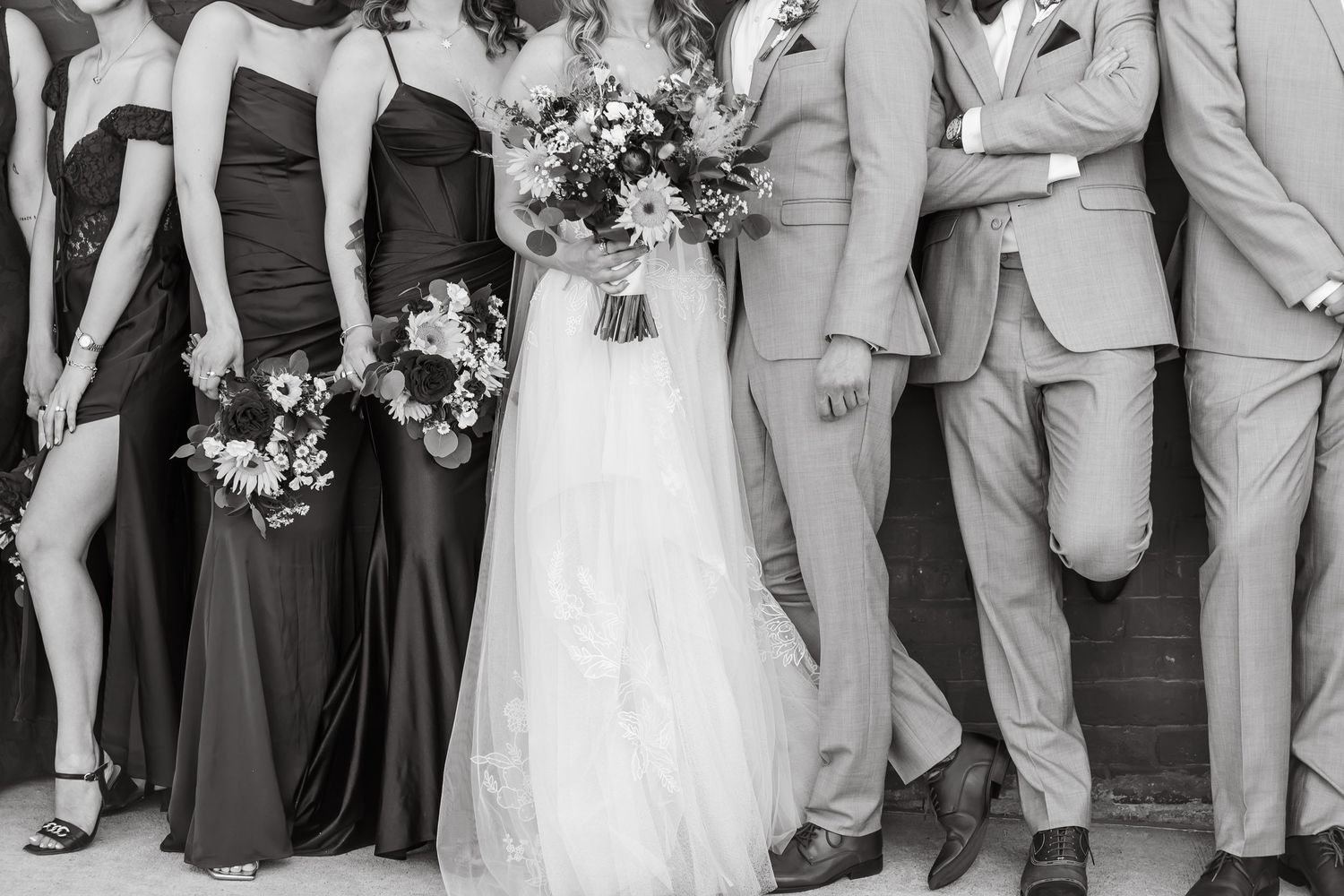 Black and white wedding party photo showing bride in white gown with bridesmaids in dark dresses and groomsmen in suits.