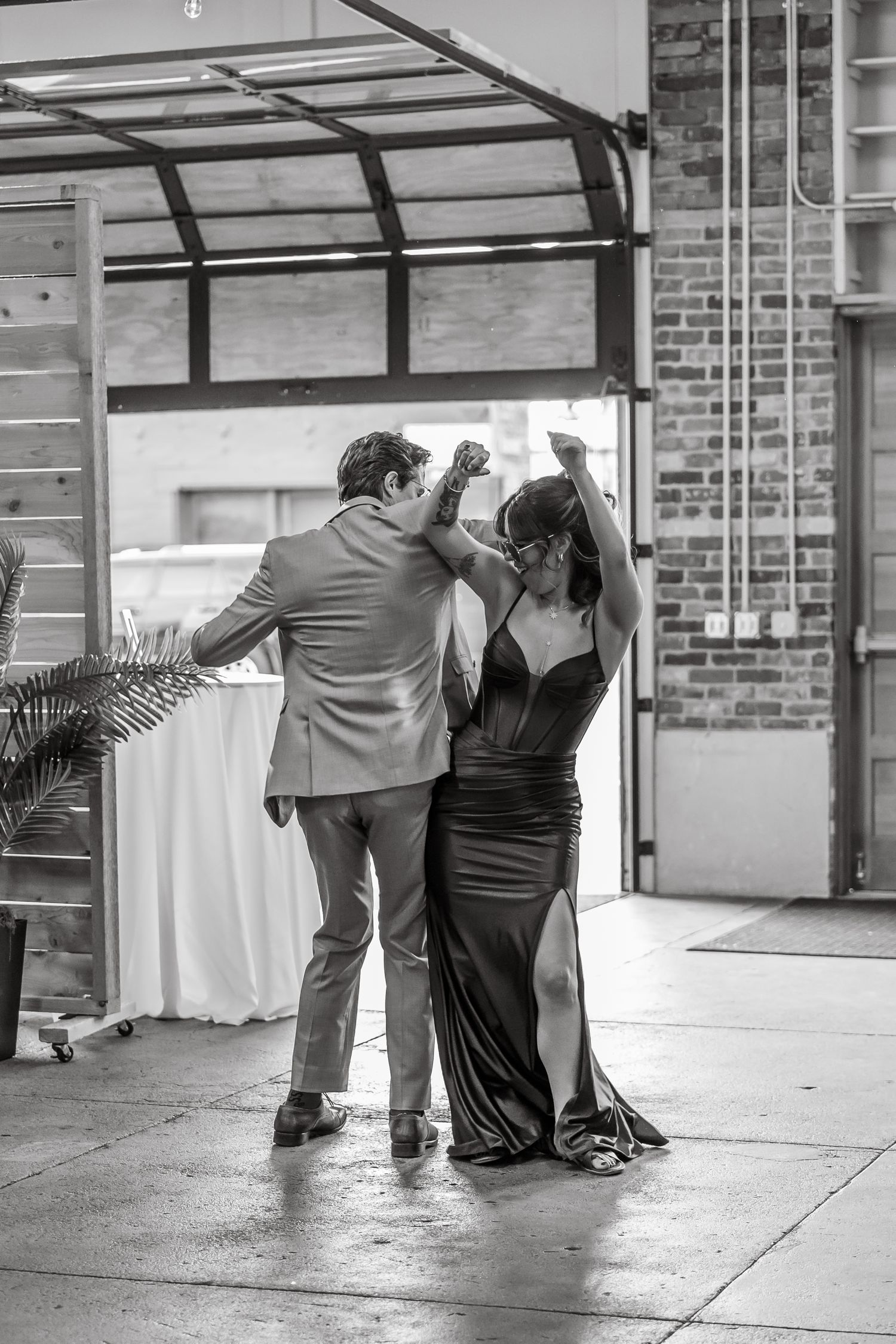 Couple dancing elegantly in black and white, man in suit twirling woman in black gown at indoor venue.