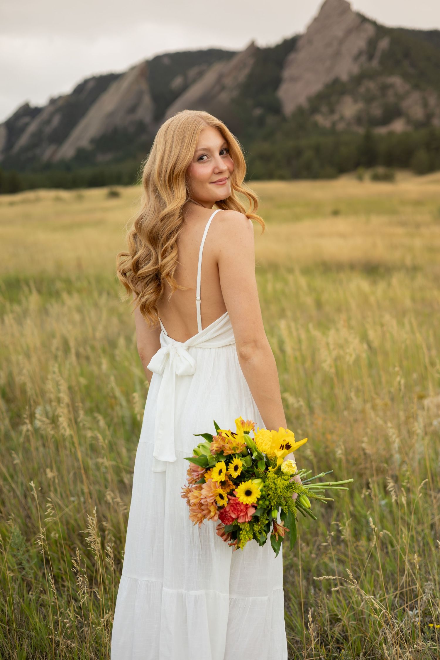 White sundress portrait with wildflower bouquet against mountain backdrop.