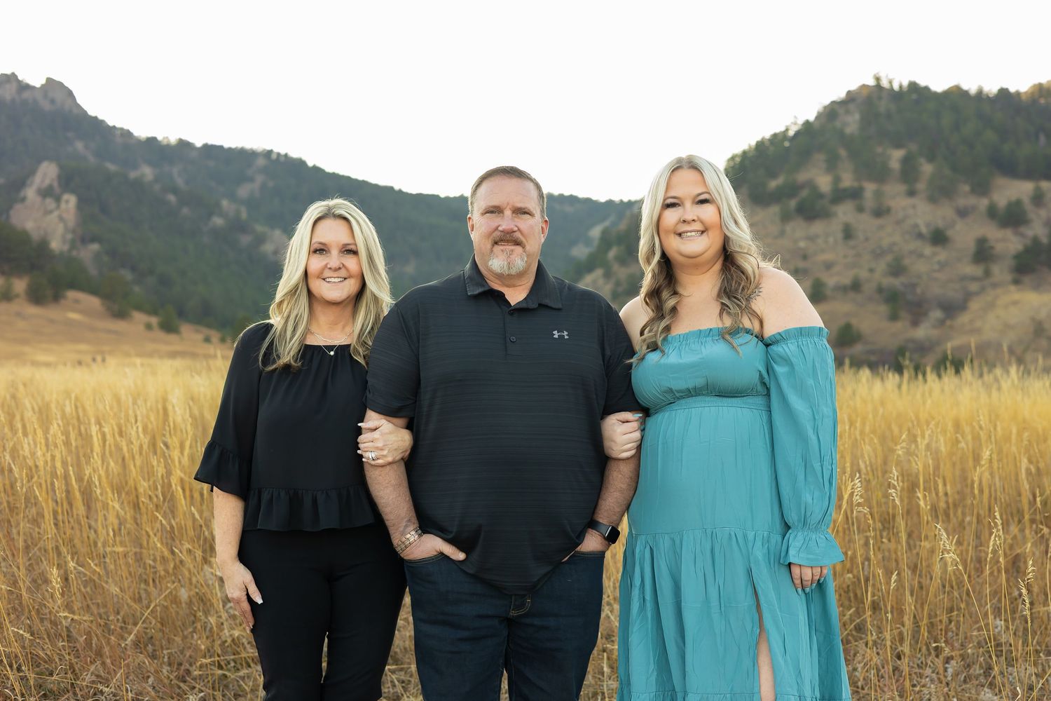 Family standing together in front of mountain landscape wearing coordinated outfits at sunset.