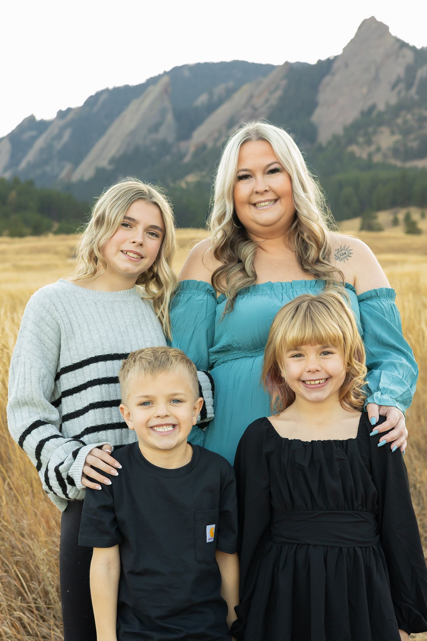 Family portrait session in a golden field with mountain backdrop wearing coordinated black and teal outfits.