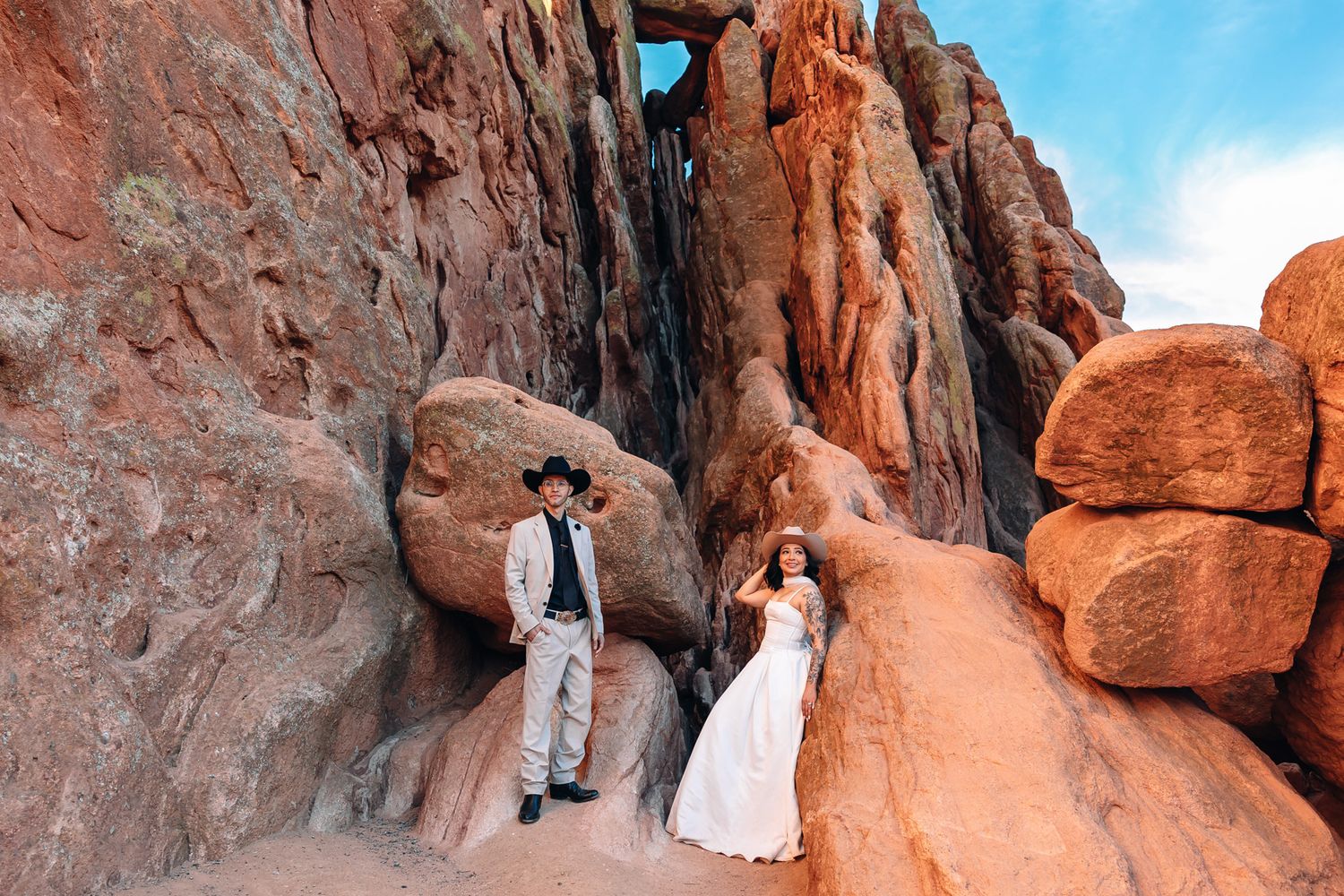 Couple in wedding attire posing among red rock formations in a desert canyon landscape.