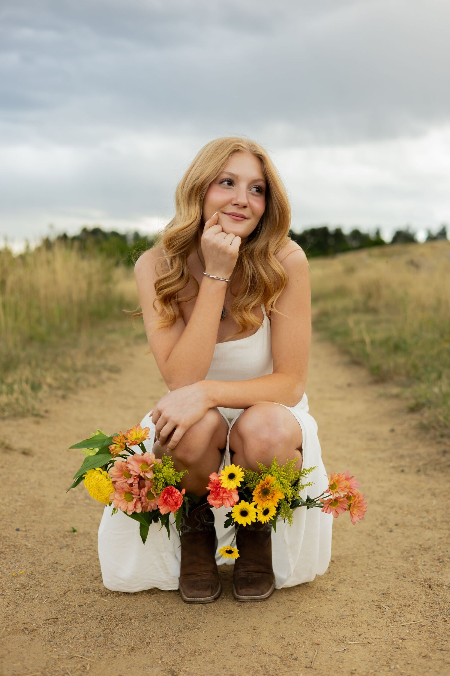 Sitting on trail with boots and sunflower bouquet against mountain landscape.