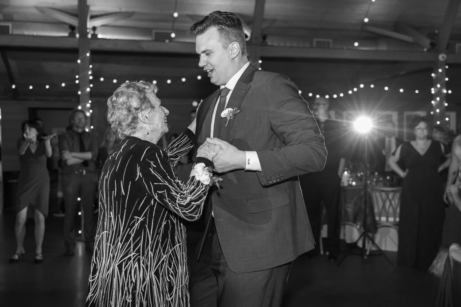 Dancing couples in formal attire under twinkling lights at an indoor venue.