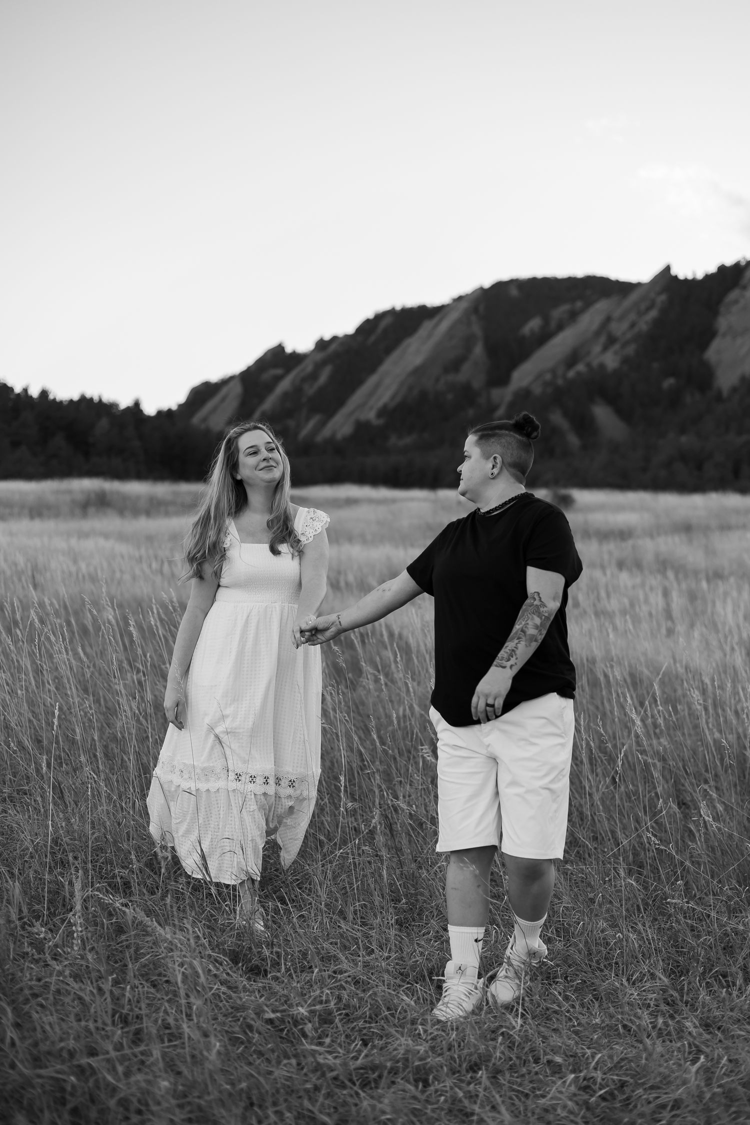 Black and white photo of a playful couple dancing in a mountain field.