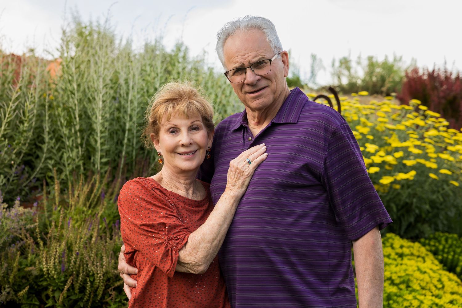 Elderly couple shares tender moments in a vibrant garden filled with yellow flowers and greenery.