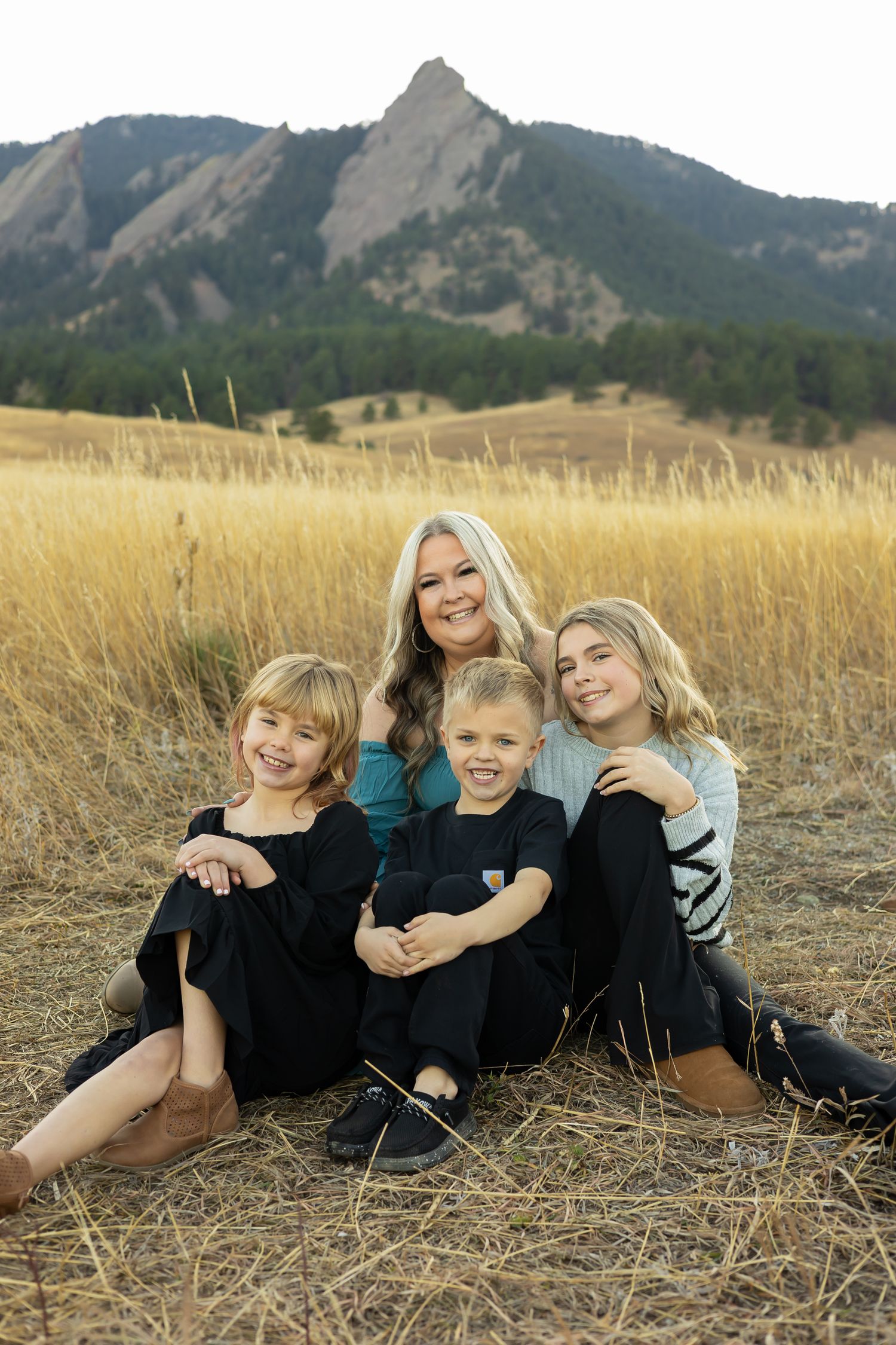 A family group poses together in a field with the iconic Flatirons mountains of Boulder behind them.