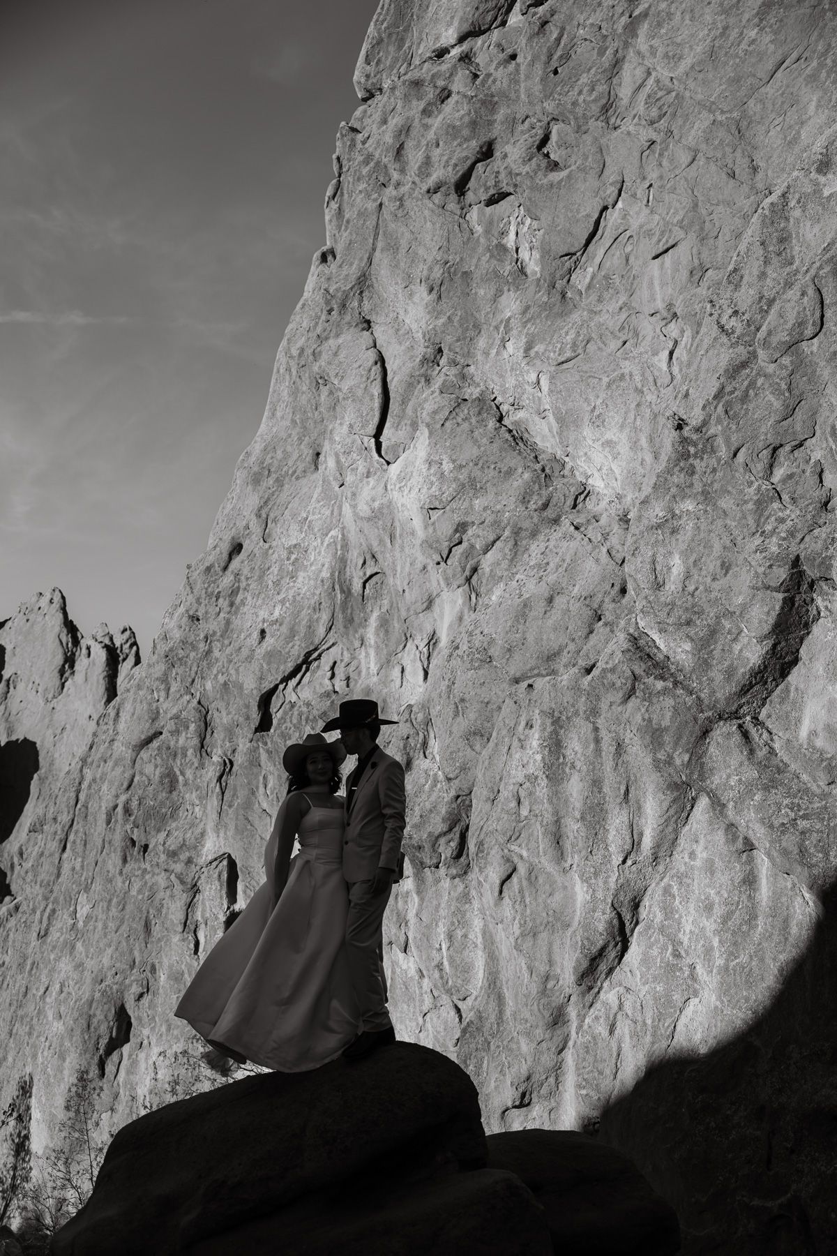 Black and white photo of a bride and groom silhouetted against dramatic rocky cliffs during an outdoor wedding.