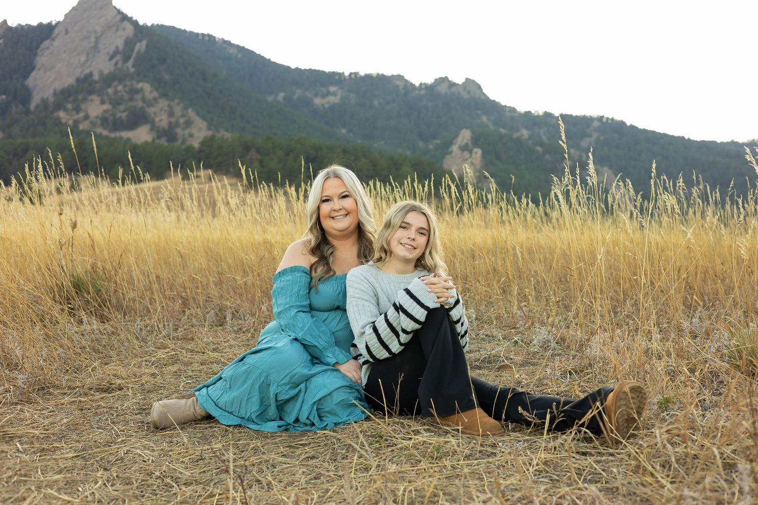 Two people in coordinating outfits pose in a golden field with mountain backdrop.