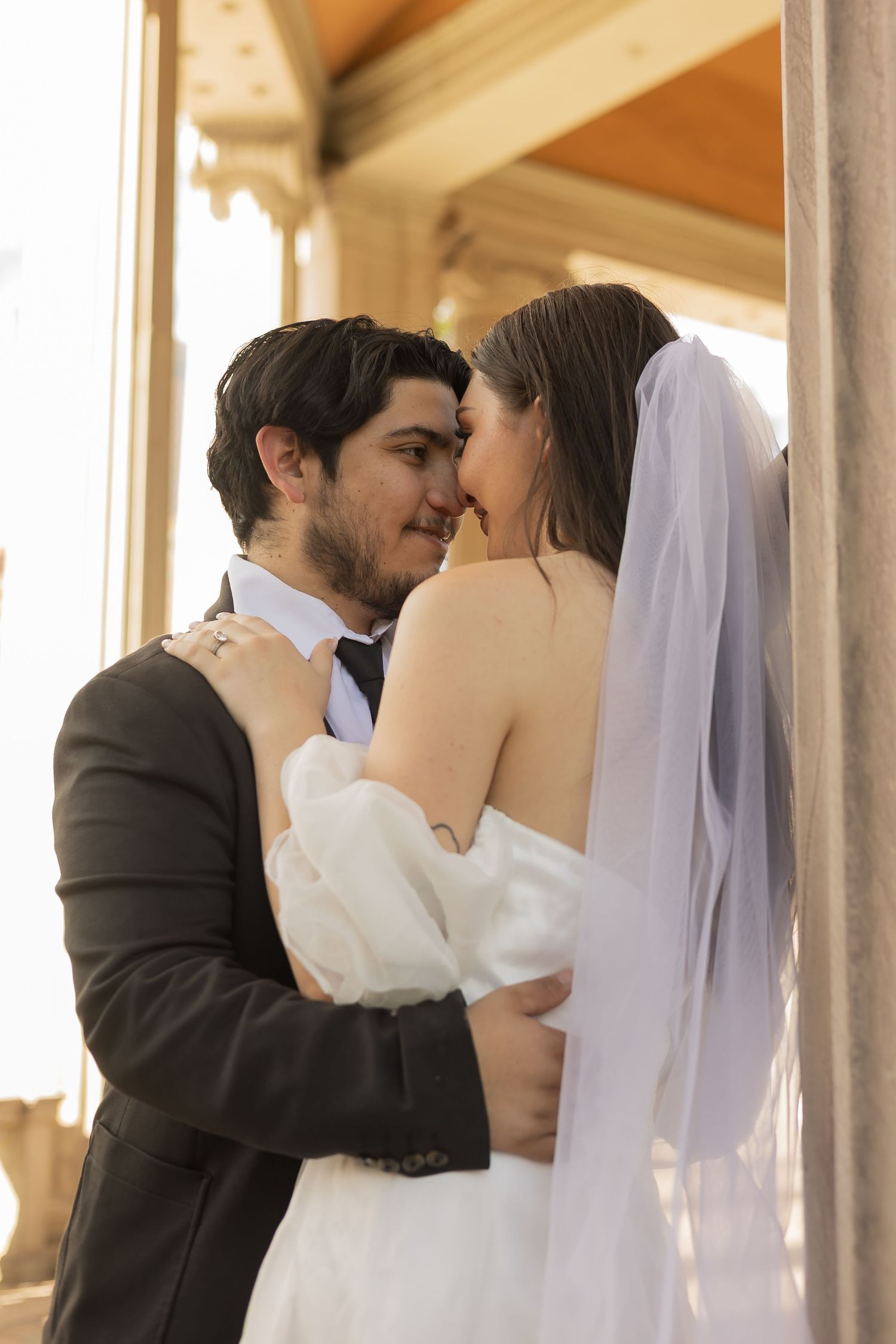 An intimate moment between newlyweds captured in warm sunlight under a covered walkway.