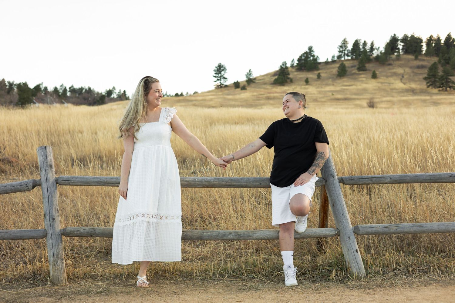 Couple sitting on wooden fence in mountain meadow during sunset.