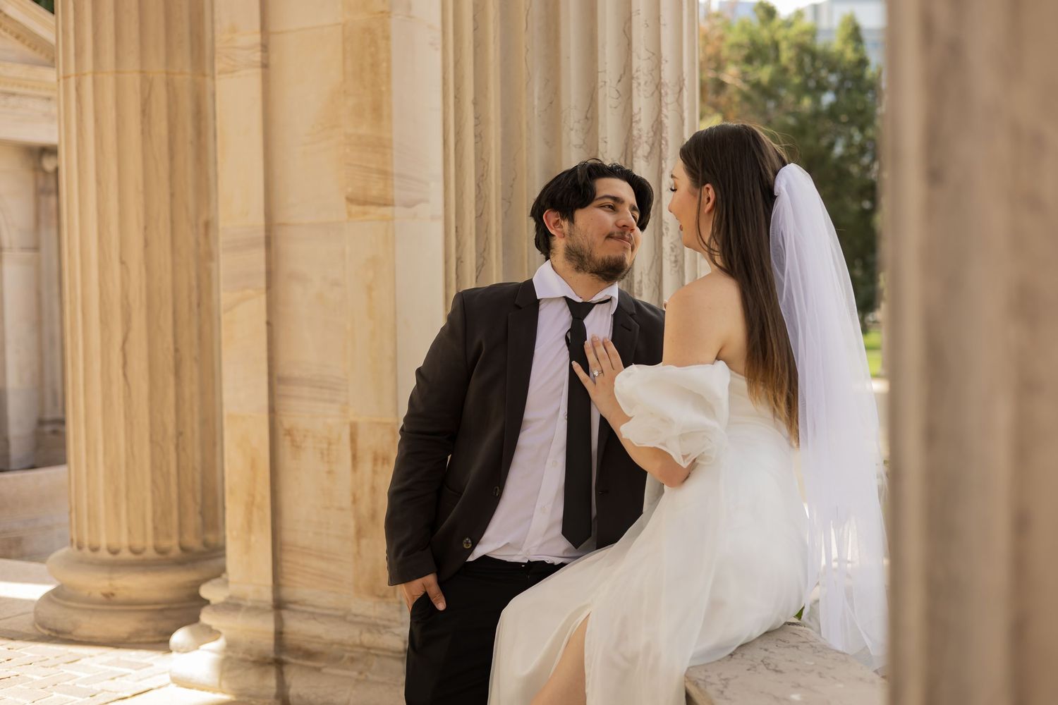 Romantic wedding moments captured between stone columns in warm sunlight.