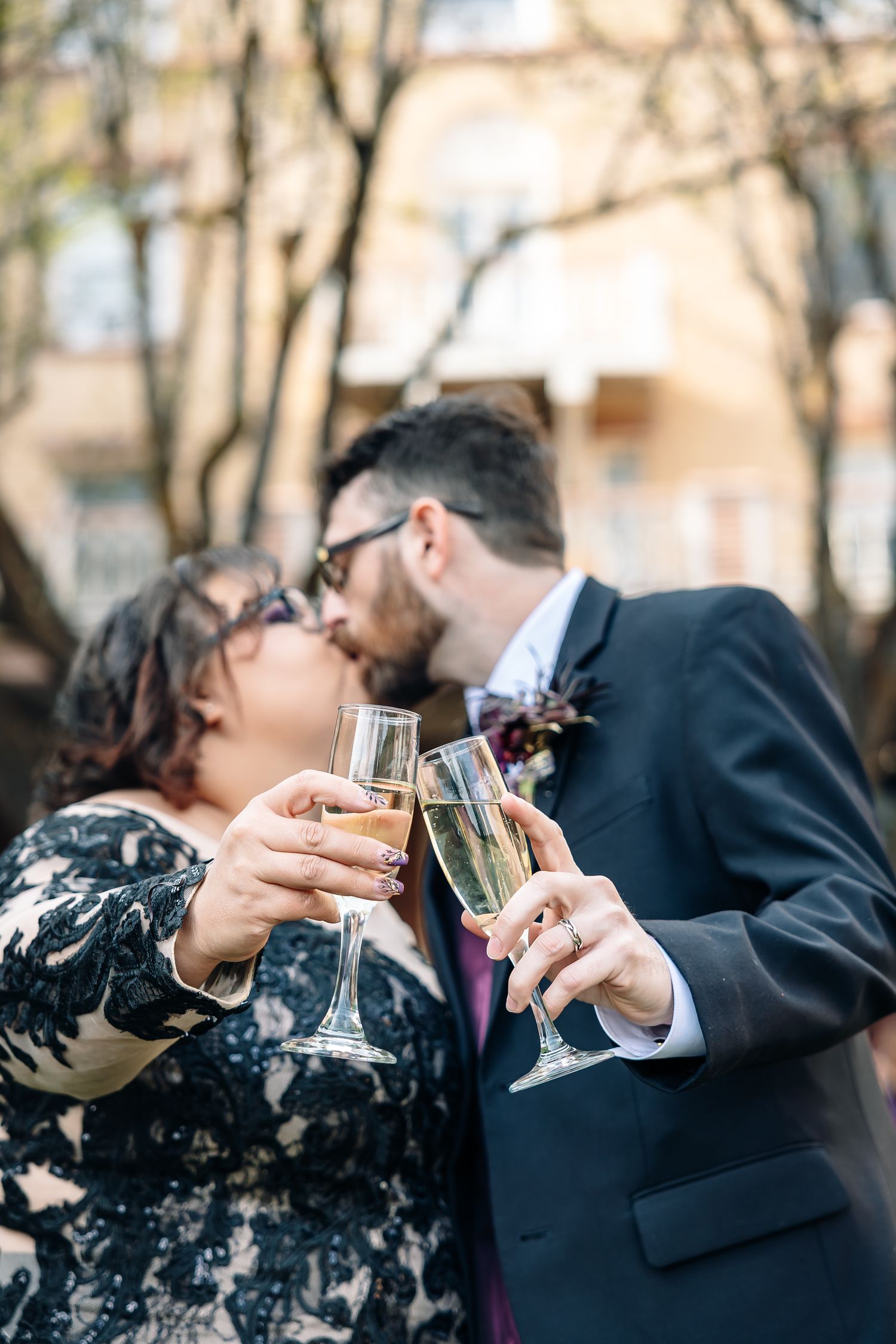 Couple kissing while toasting with champagne glasses outdoors at their wedding celebration.