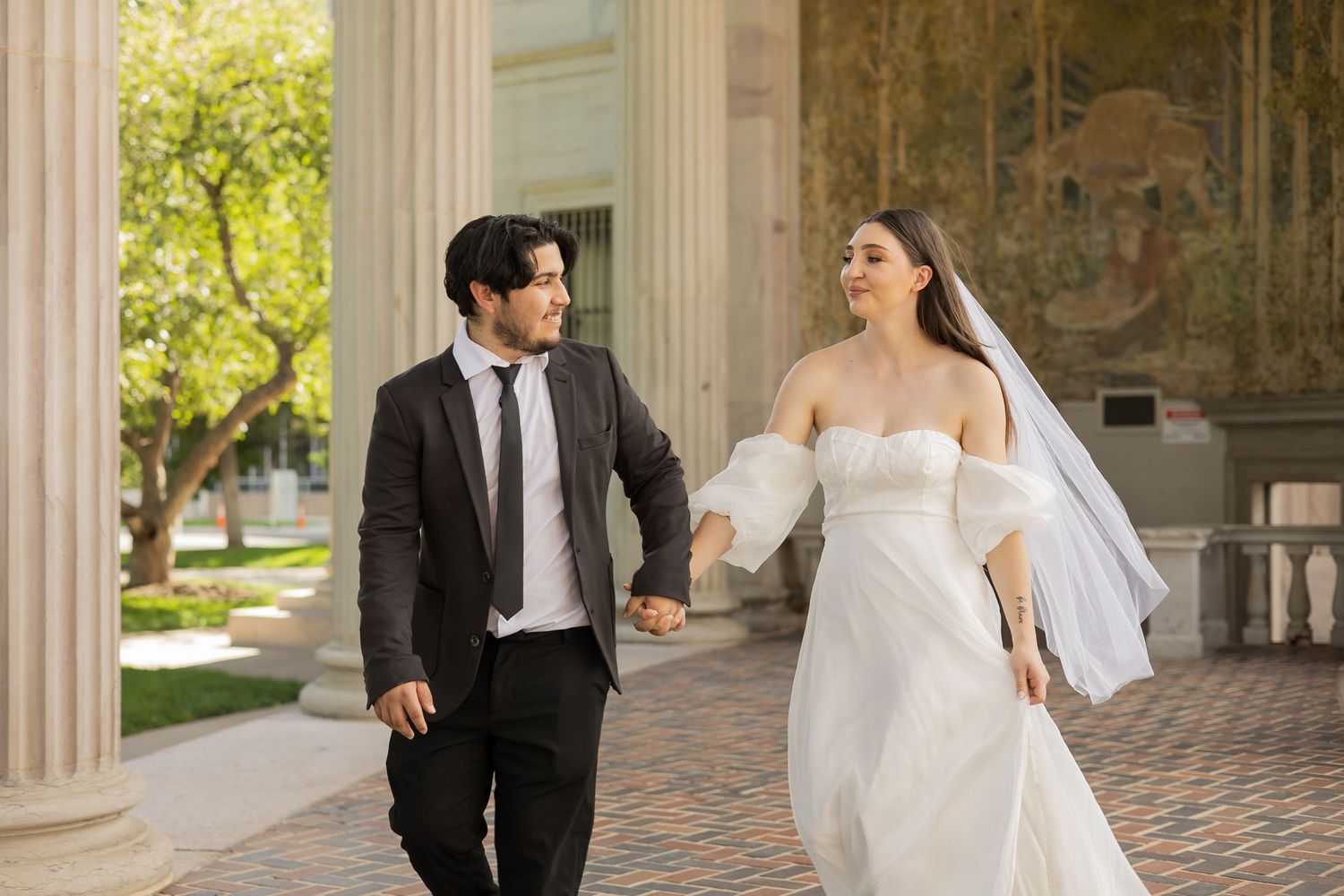 Wedding couple poses playfully under stone archway during photo session.