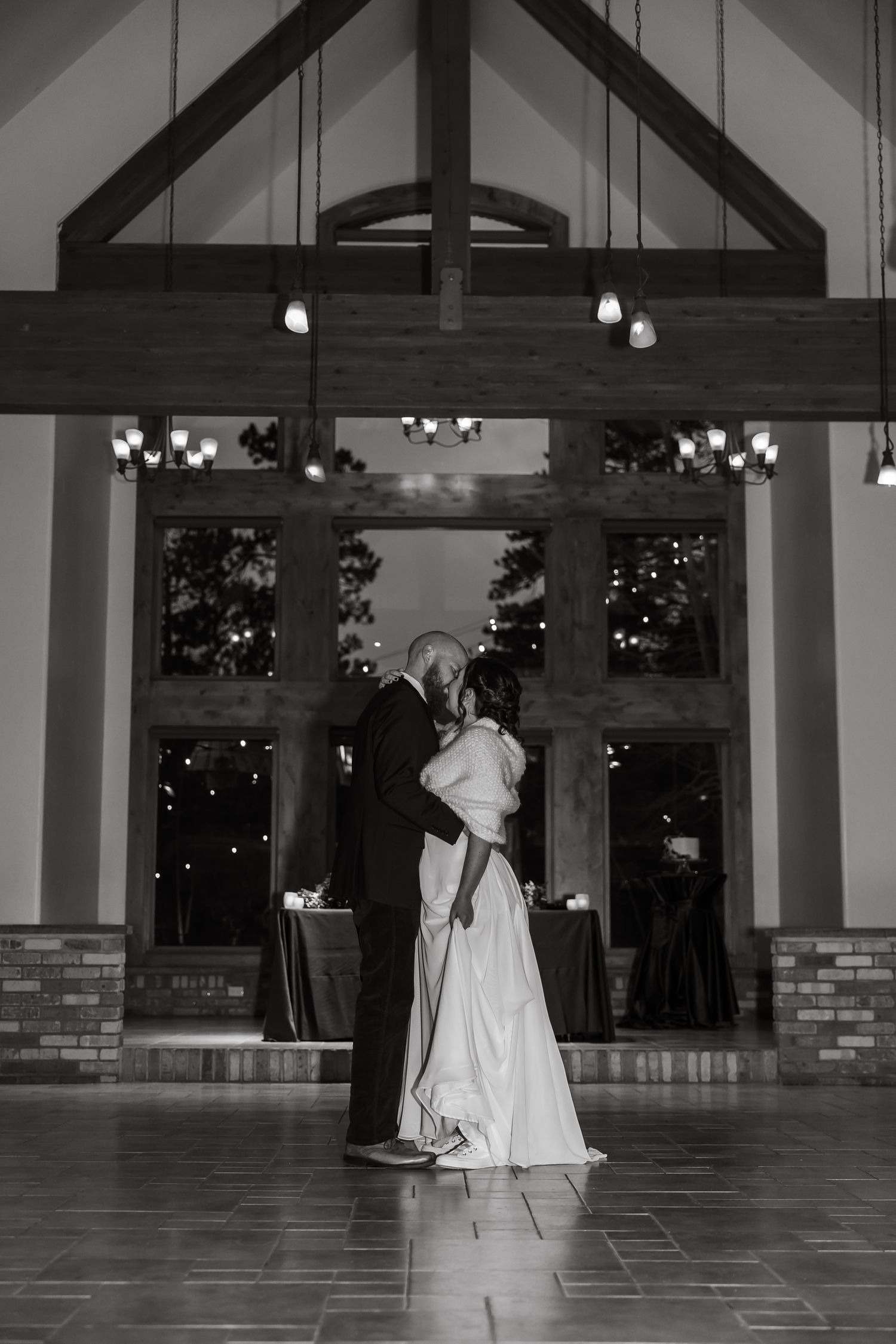 Bride and groom share first dance in elegant rustic wedding venue in black and white photo.