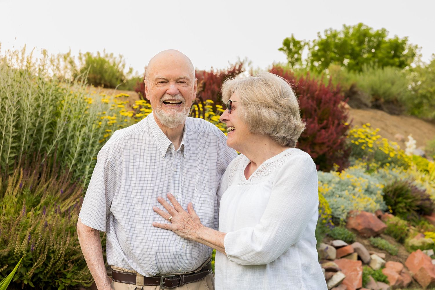 Senior couple embraces while enjoying a sunny day in a colorful garden landscape.