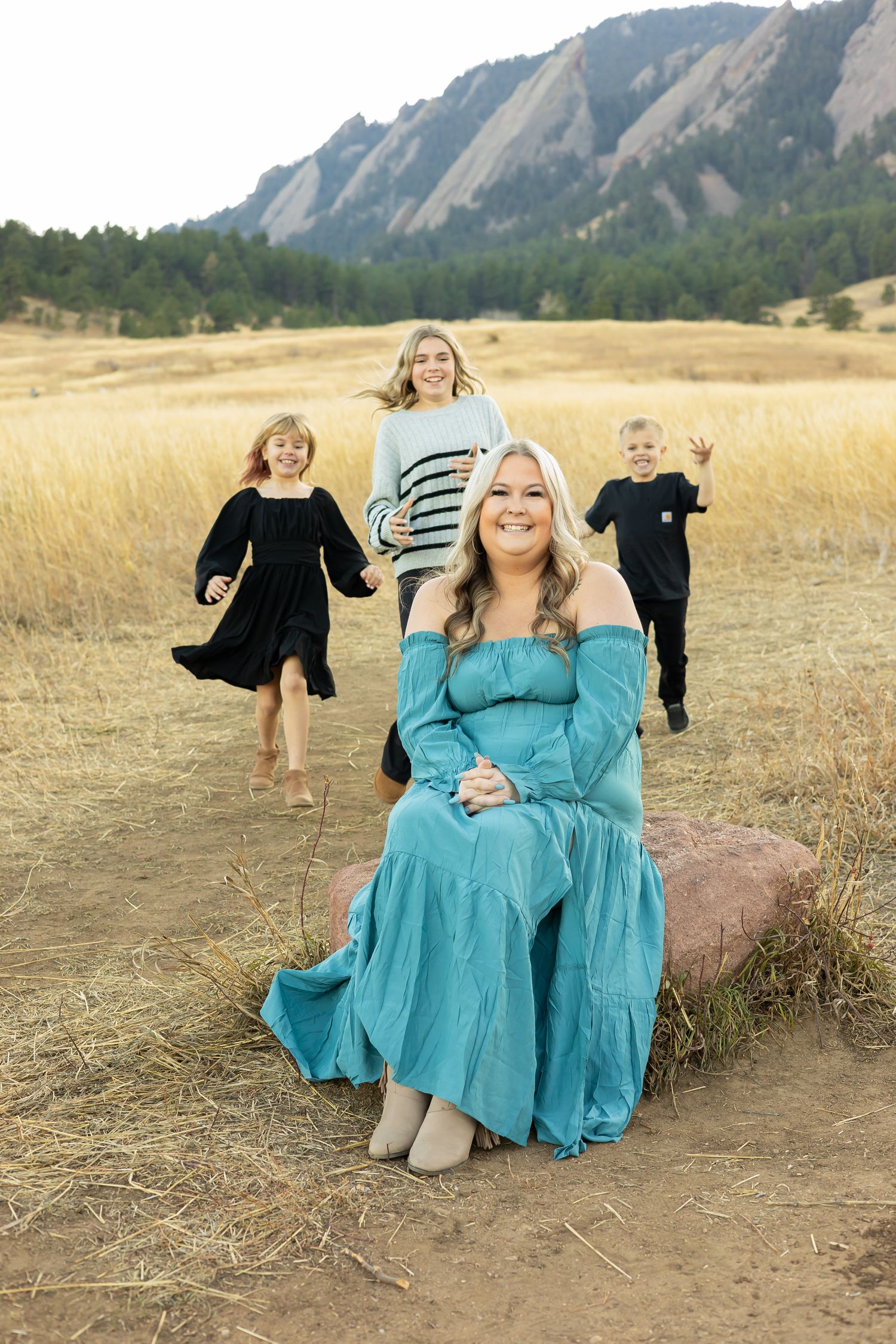 A family plays in a golden field with the dramatic Flatirons rock formation in the background.