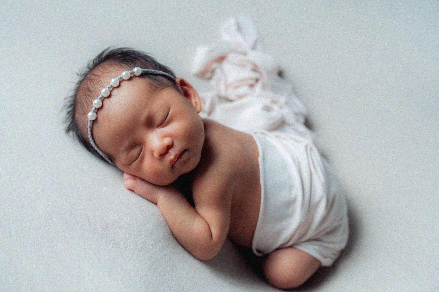 Sleeping newborn in white wrap positioned on light blue background.