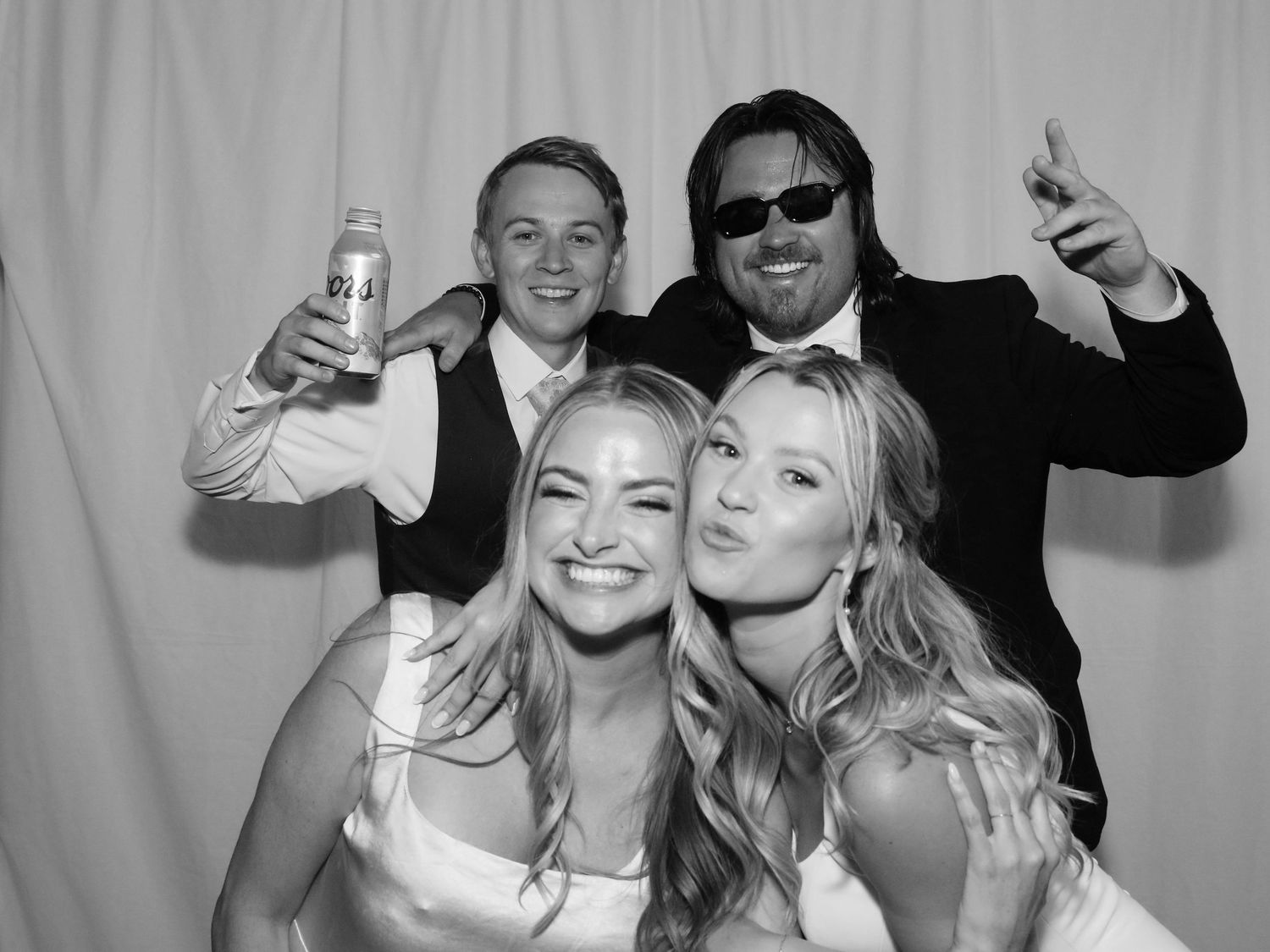 Black and white photo booth picture of four friends posing and celebrating at a wedding reception.