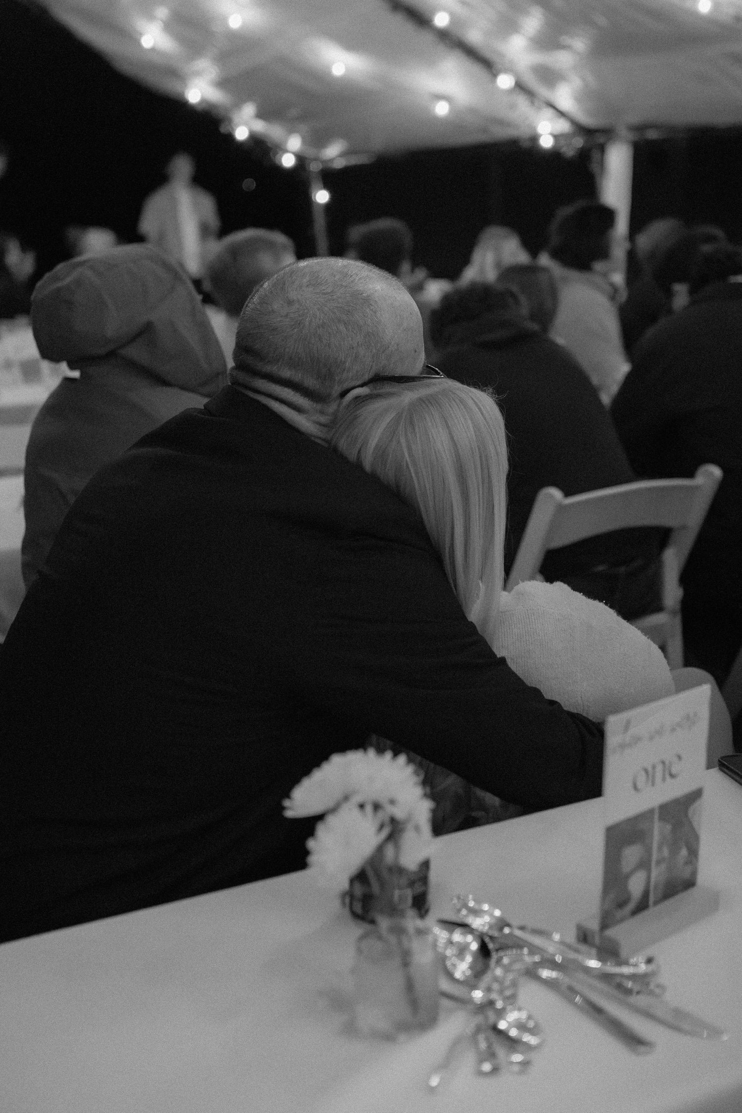 Wedding guests seated at tables in a dimly lit reception venue with decorative lighting.