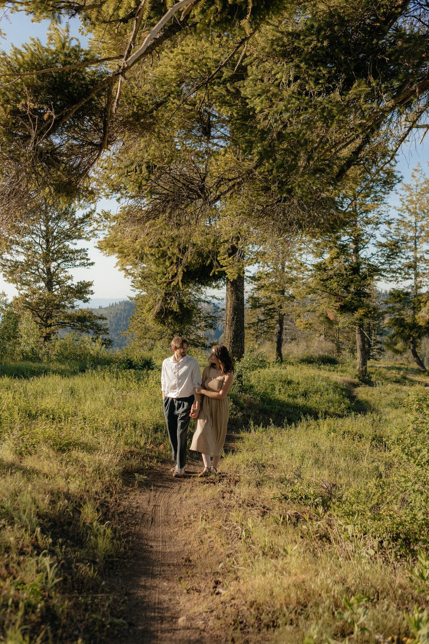 Couple walking along a scenic mountain trail surrounded by pine trees and natural beauty.