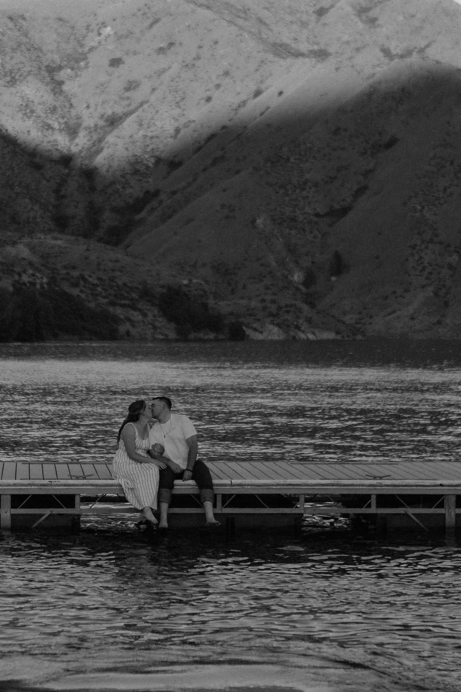 Couple sitting romantically on a dock overlooking a mountain lake at dusk.