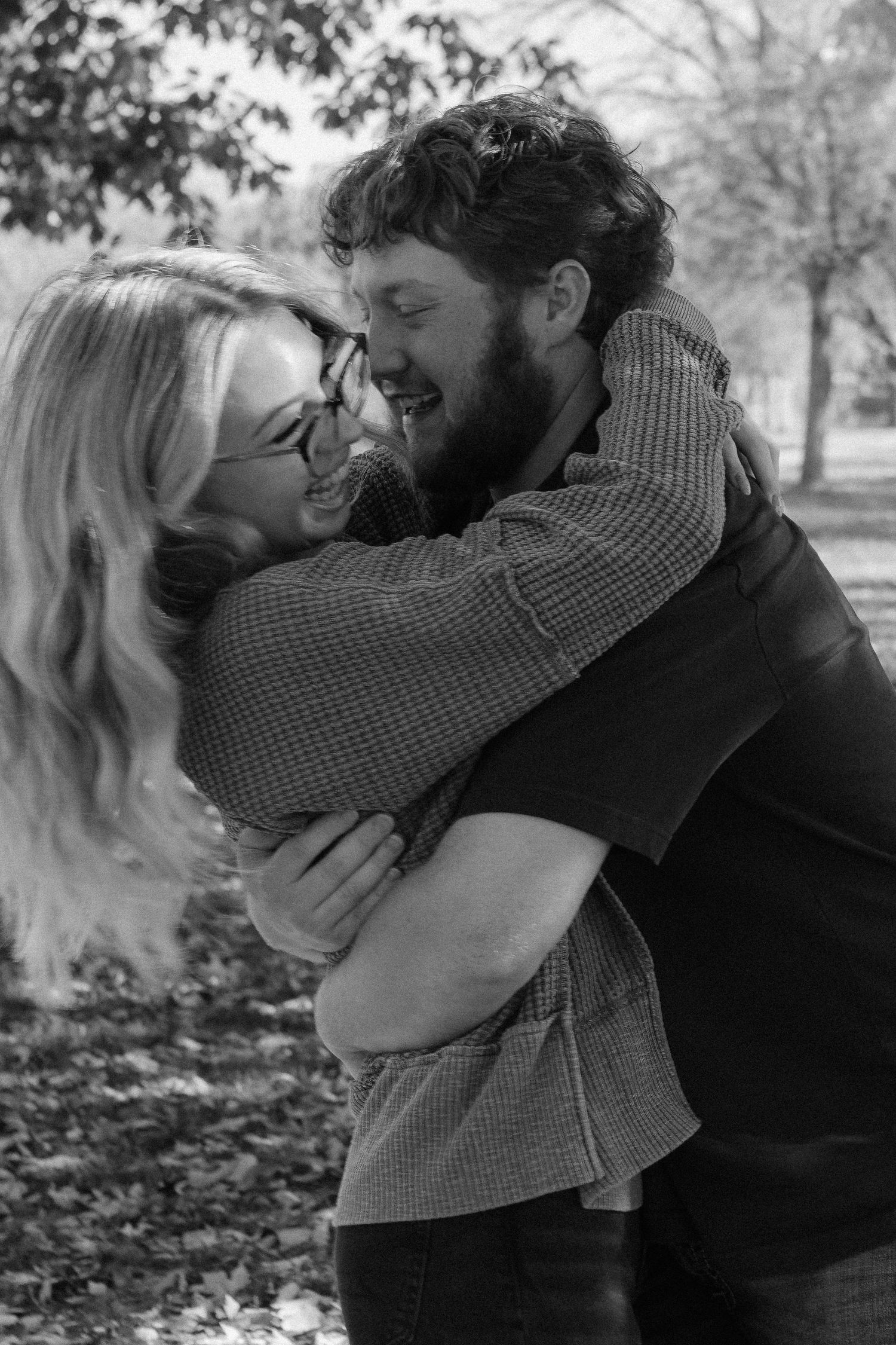 A tender embrace captured in black and white photography under autumn trees.