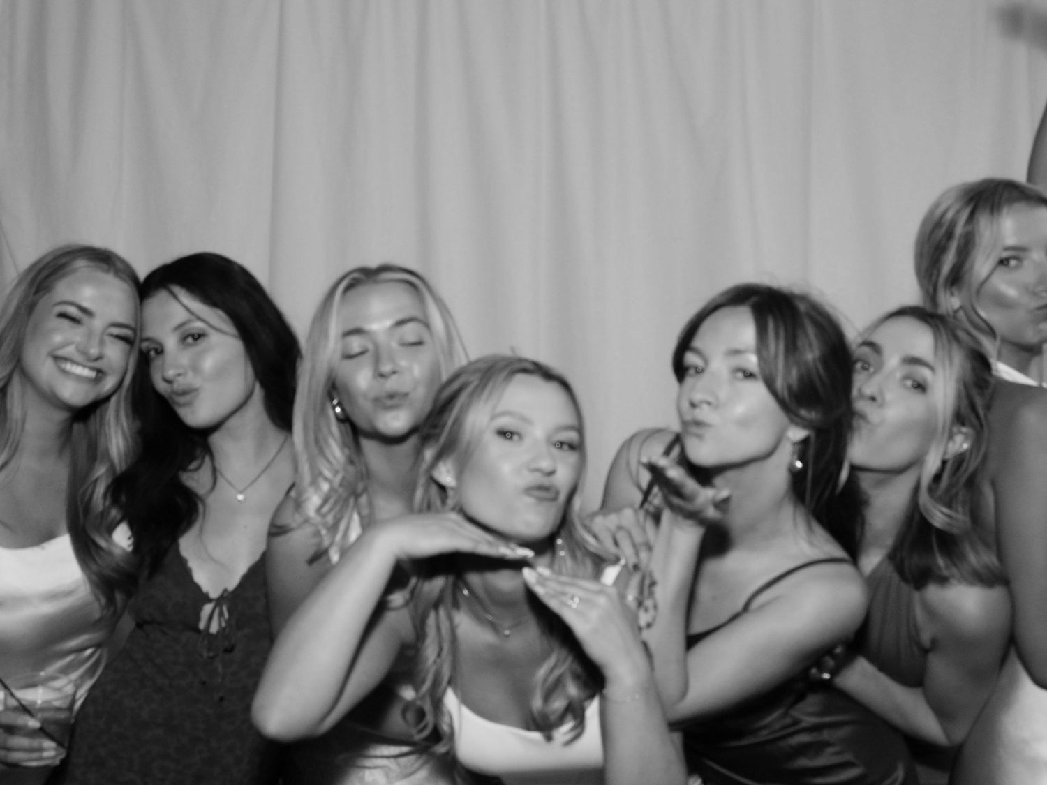 Black and white photo booth picture of a group of young women posing together, making fun faces and gestures.