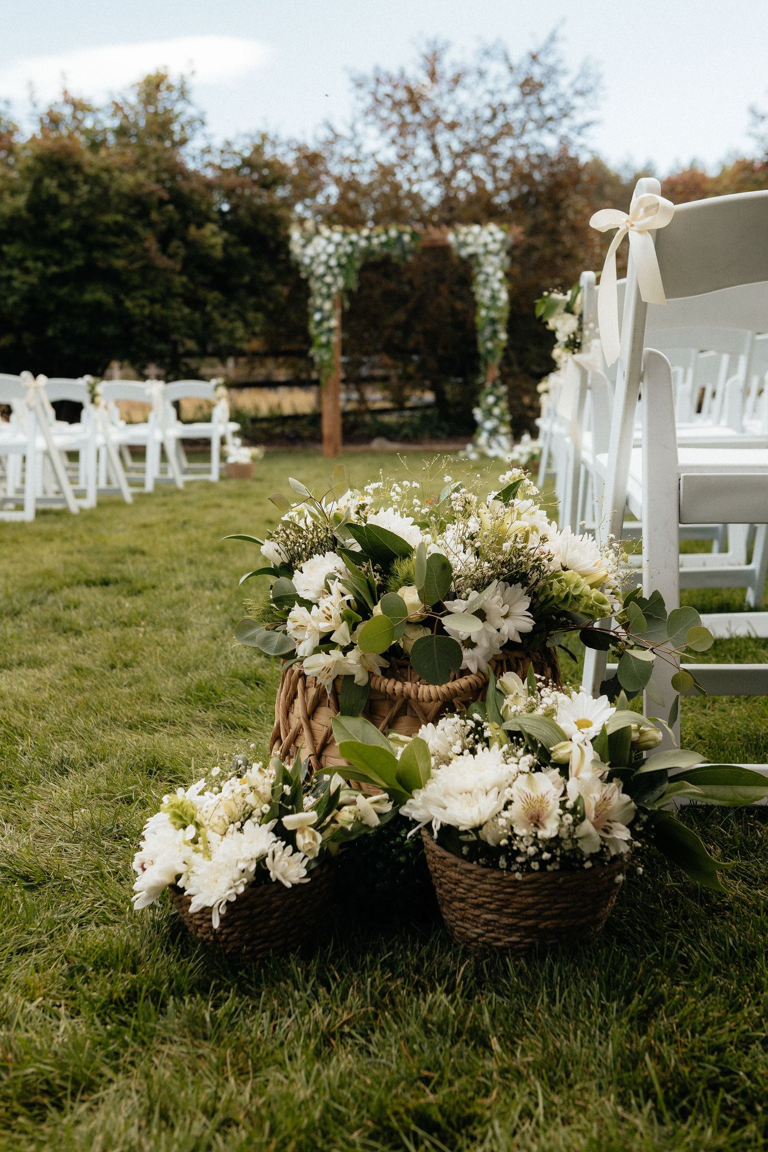 White wedding ceremony chairs decorated with floral arrangements and ribbons on a grassy lawn.