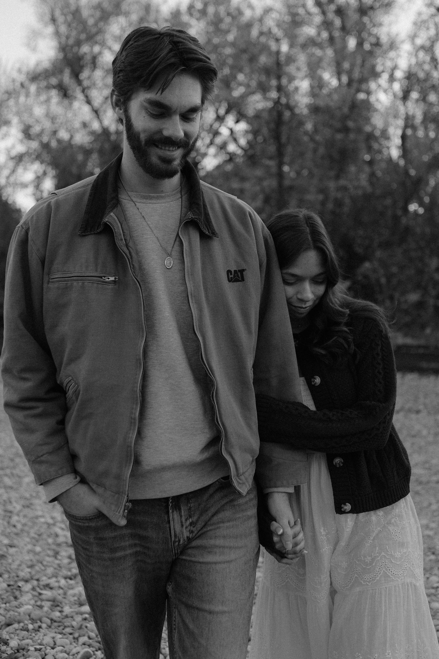 Black and white photo of couple walking together through fallen leaves.