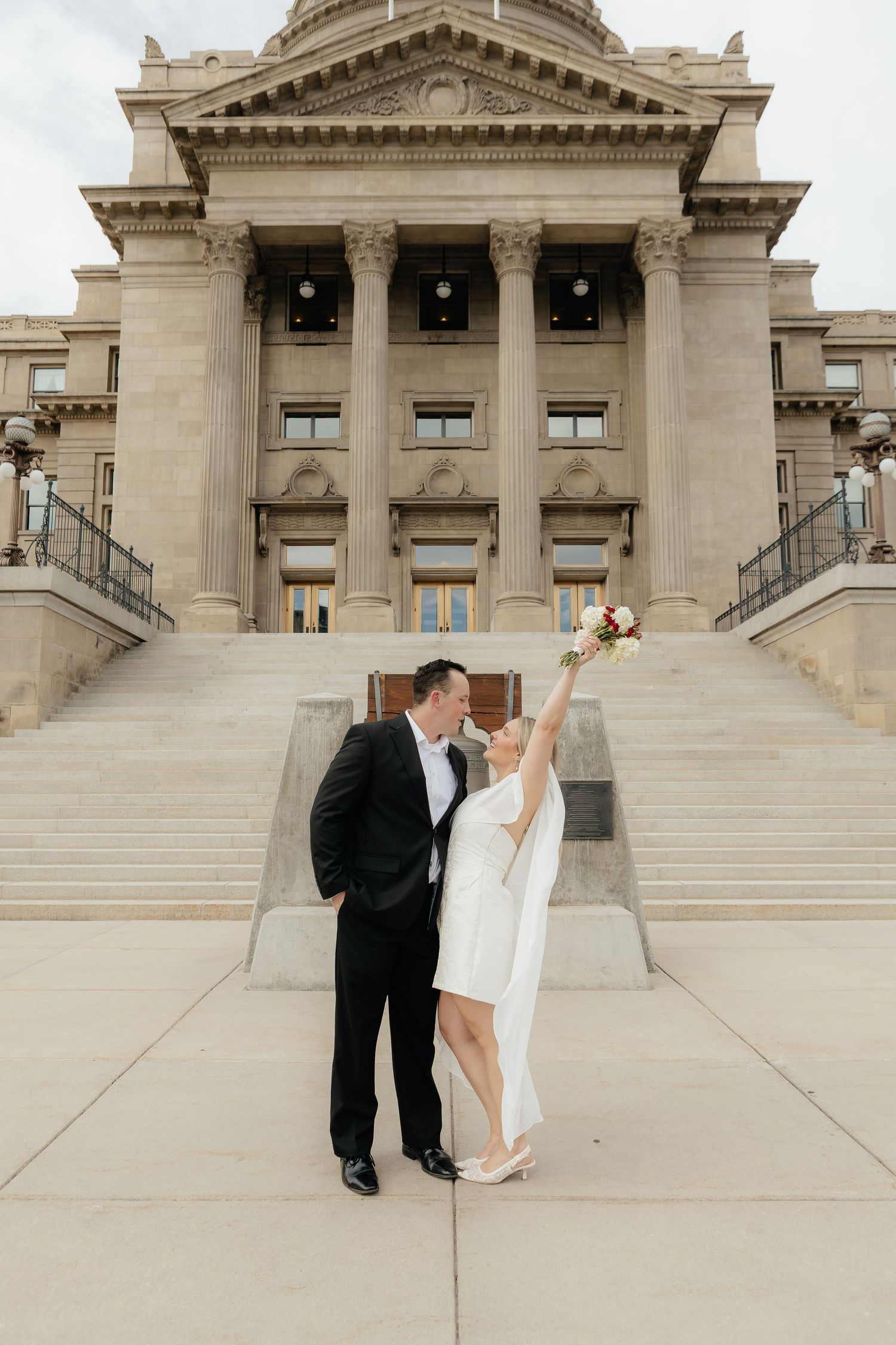 A wedding photoshoot on the grand steps of a neoclassical government building with stone columns and architecture.