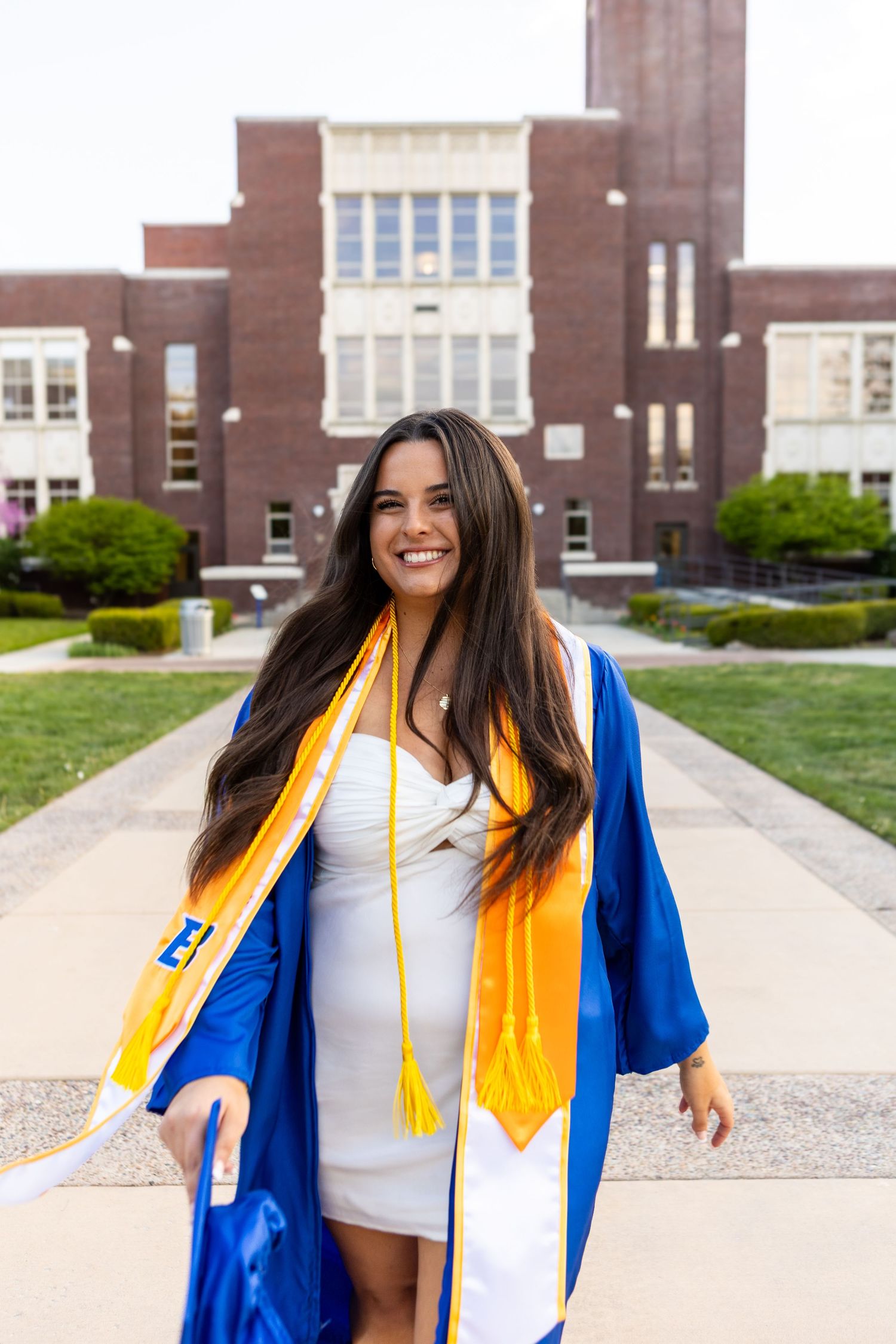 Graduate in academic regalia poses in front of brick university building.