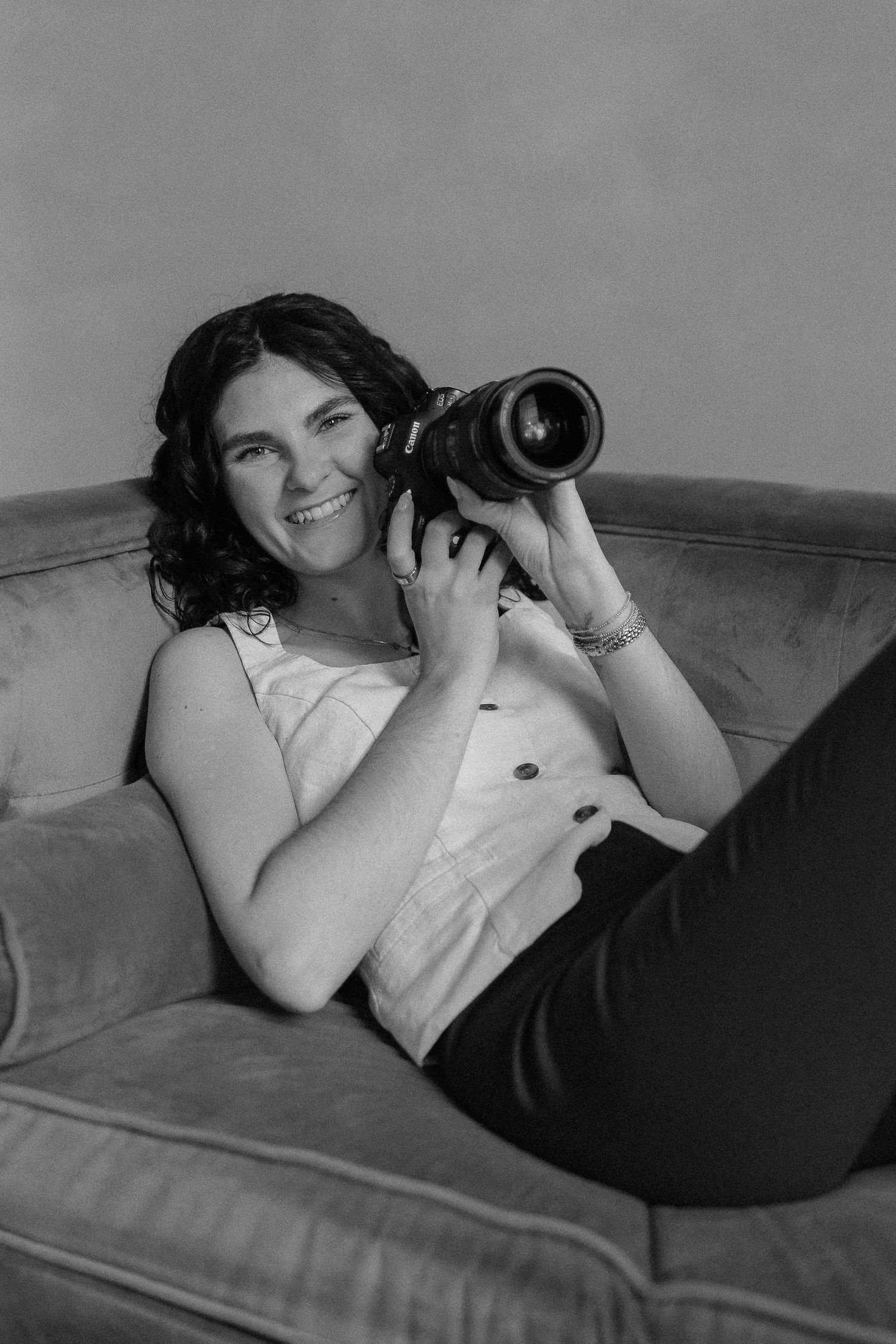 Black and white portrait of a photographer lounging on a couch with a professional camera.