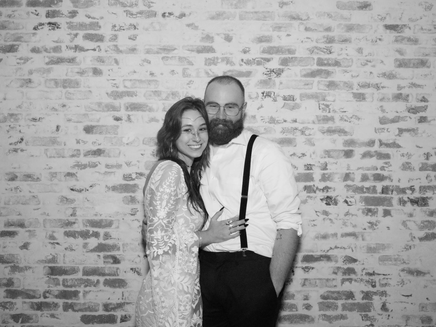 Black and white portrait of a couple in formal wedding attire against a brick wall.