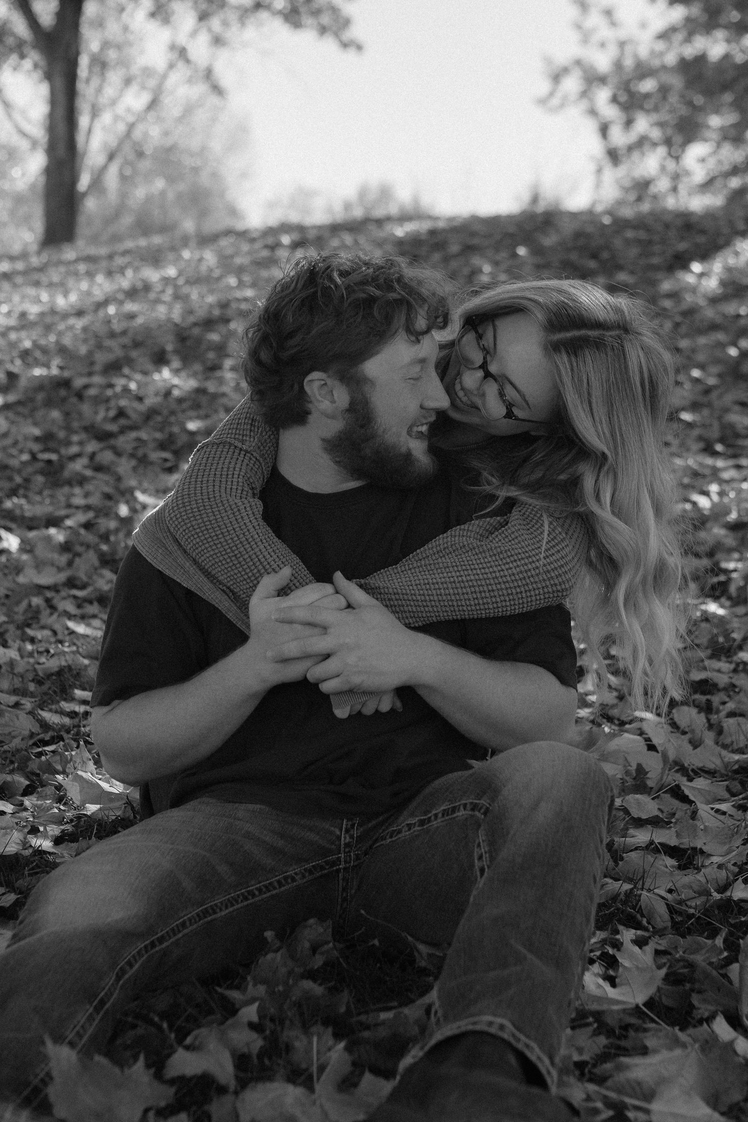 A loving couple shares a tender moment while sitting among fallen leaves.