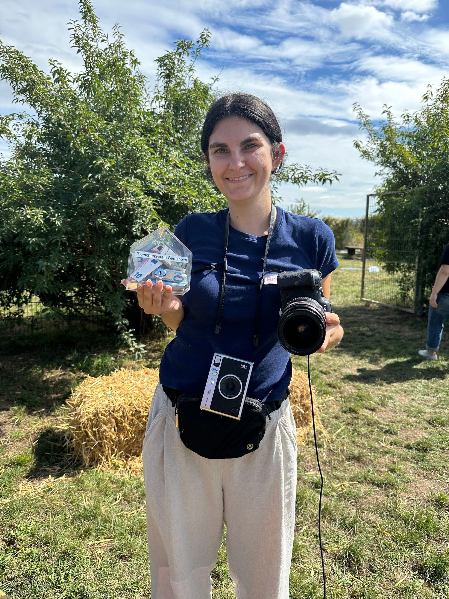 Person in navy clothing holding vintage camera in an orchard setting.