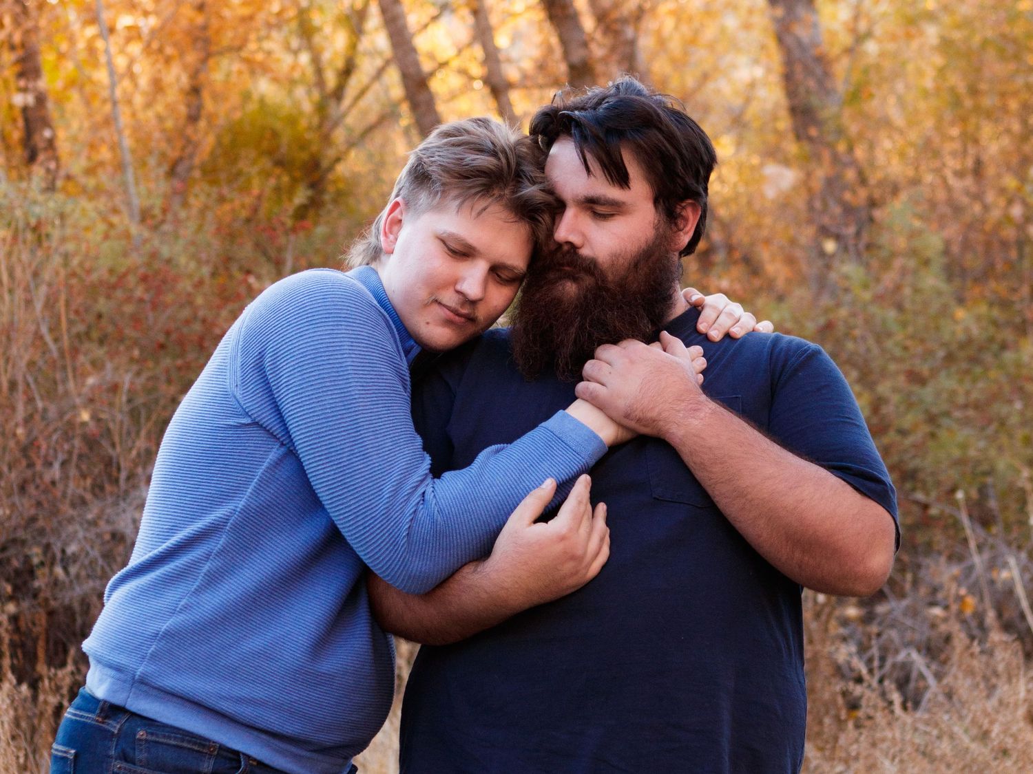 Two people in casual attire sharing an intimate moment together among autumn foliage.