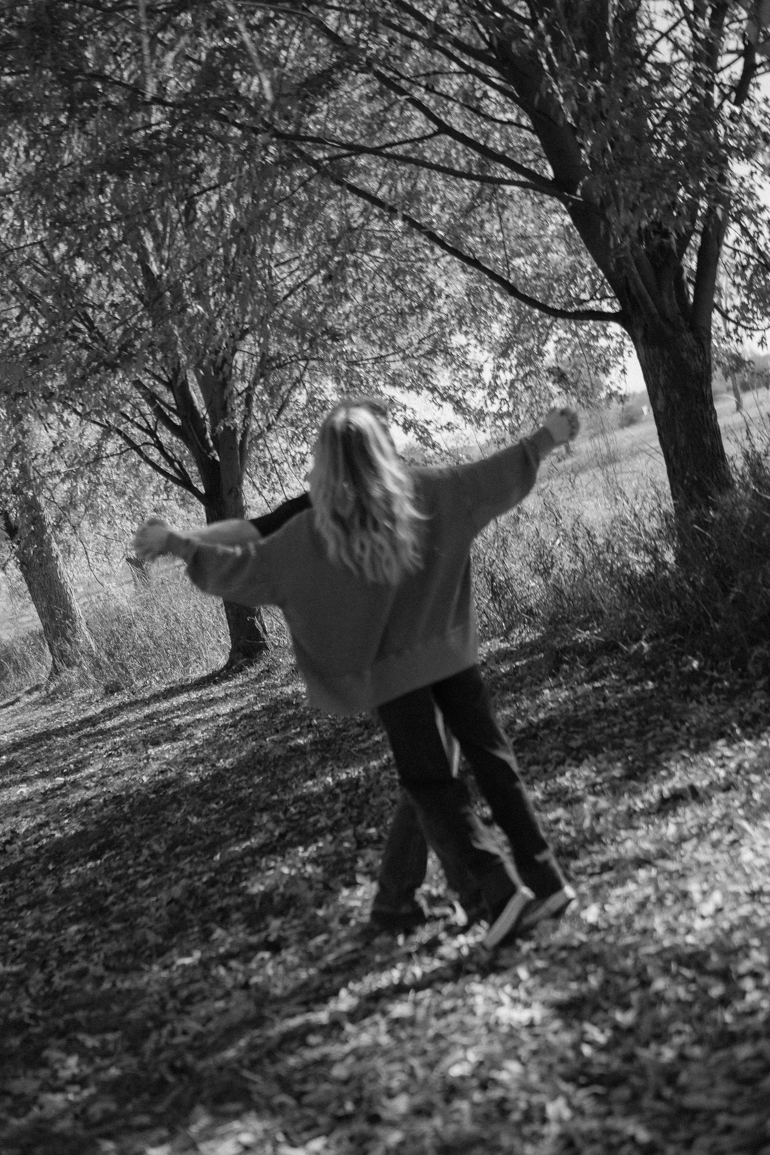 A joyful figure spins with arms outstretched beneath autumn trees in a black and white photograph.