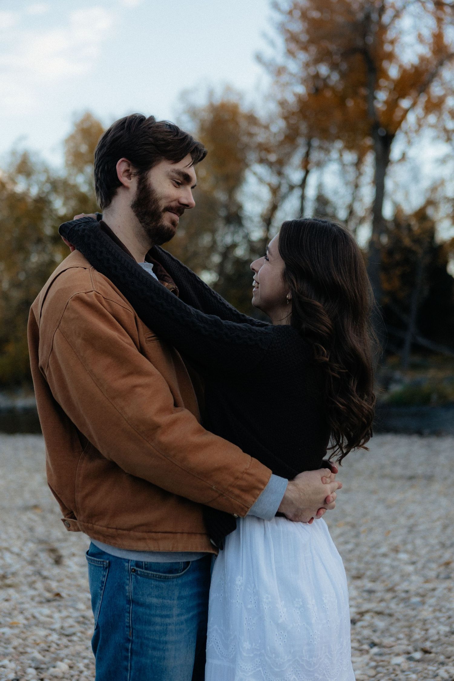 Couple embracing on rocky terrain with autumn trees in background.