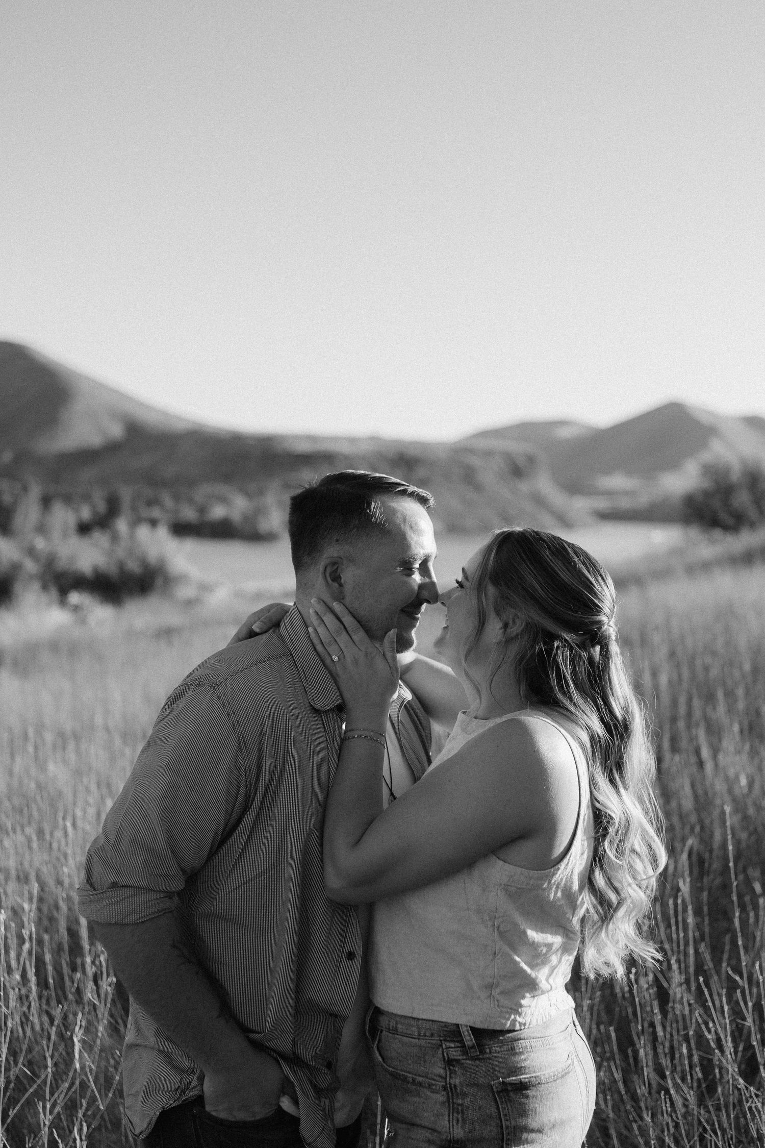 A romantic moment captured between two people in a mountain field at sunset.