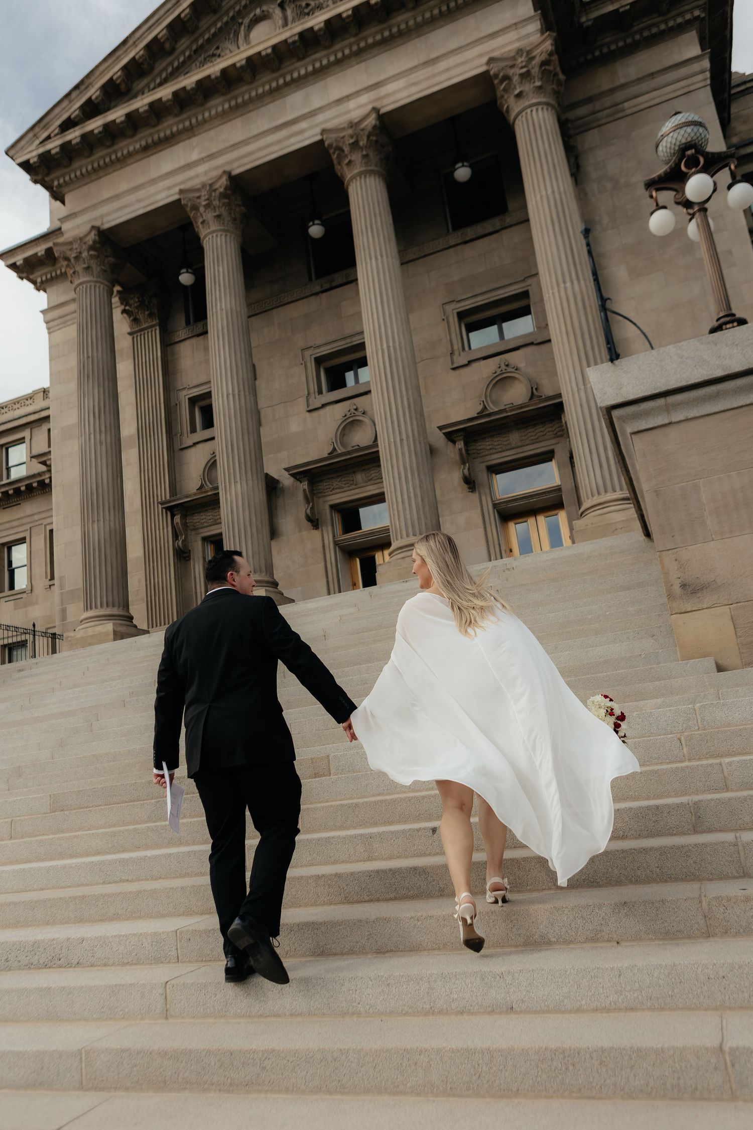 Four sequential photos show a bride and groom walking up grand stone steps of a historic building with neoclassical columns.