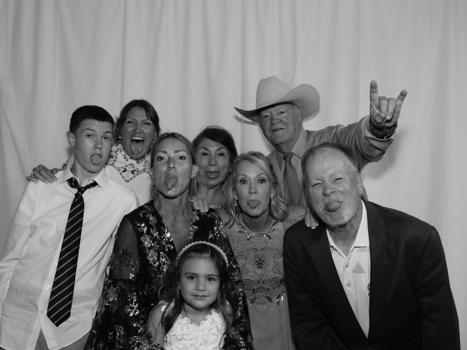 Black and white photo booth group shot of seven adults and one child making fun poses at a wedding celebration.