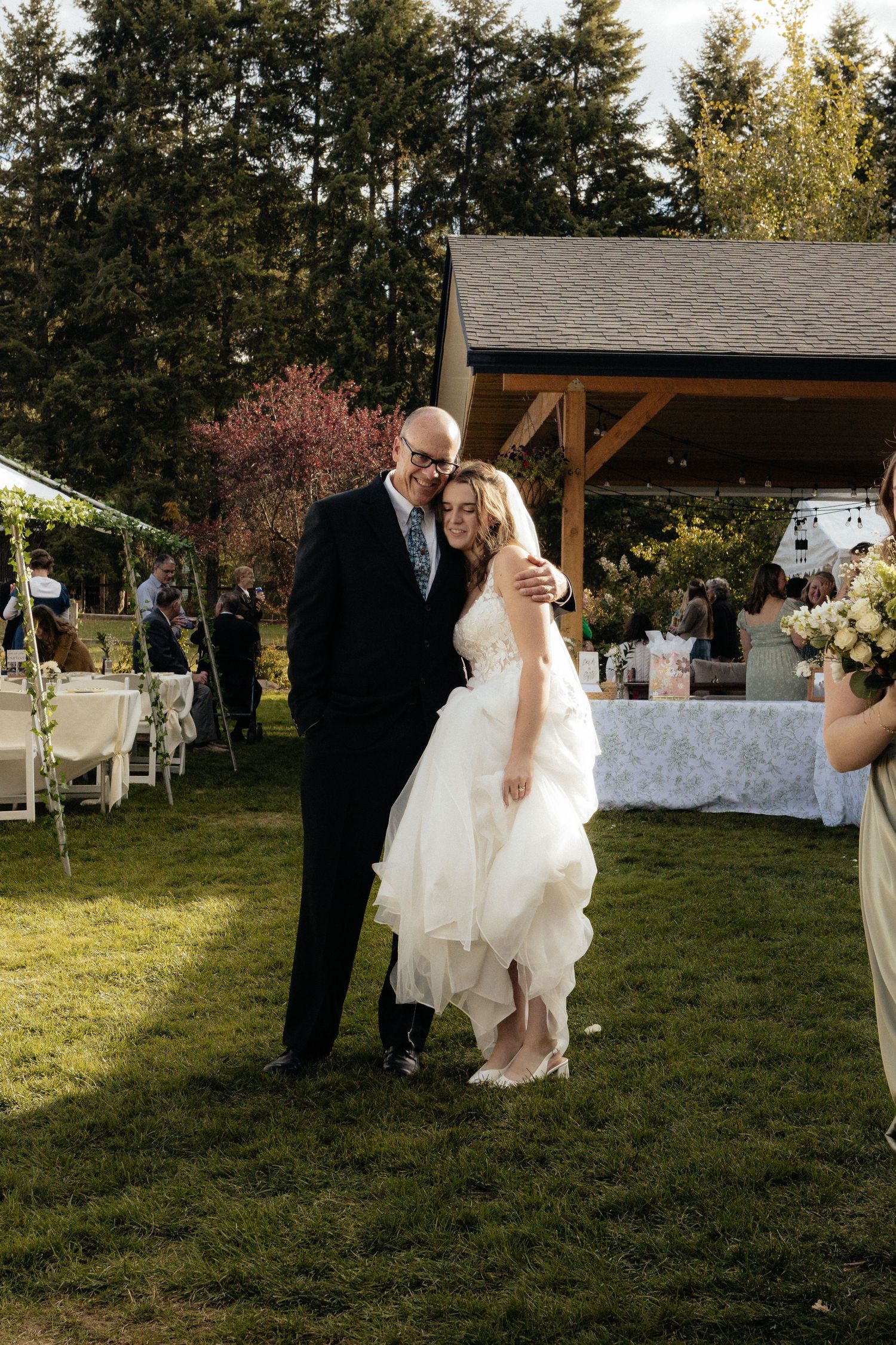 Outdoor wedding ceremony setup with wooden pavilion and white chairs on sunny lawn.