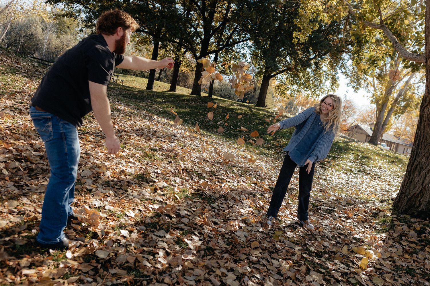 Couple walking through autumn leaves in a wooded area during a photo session.