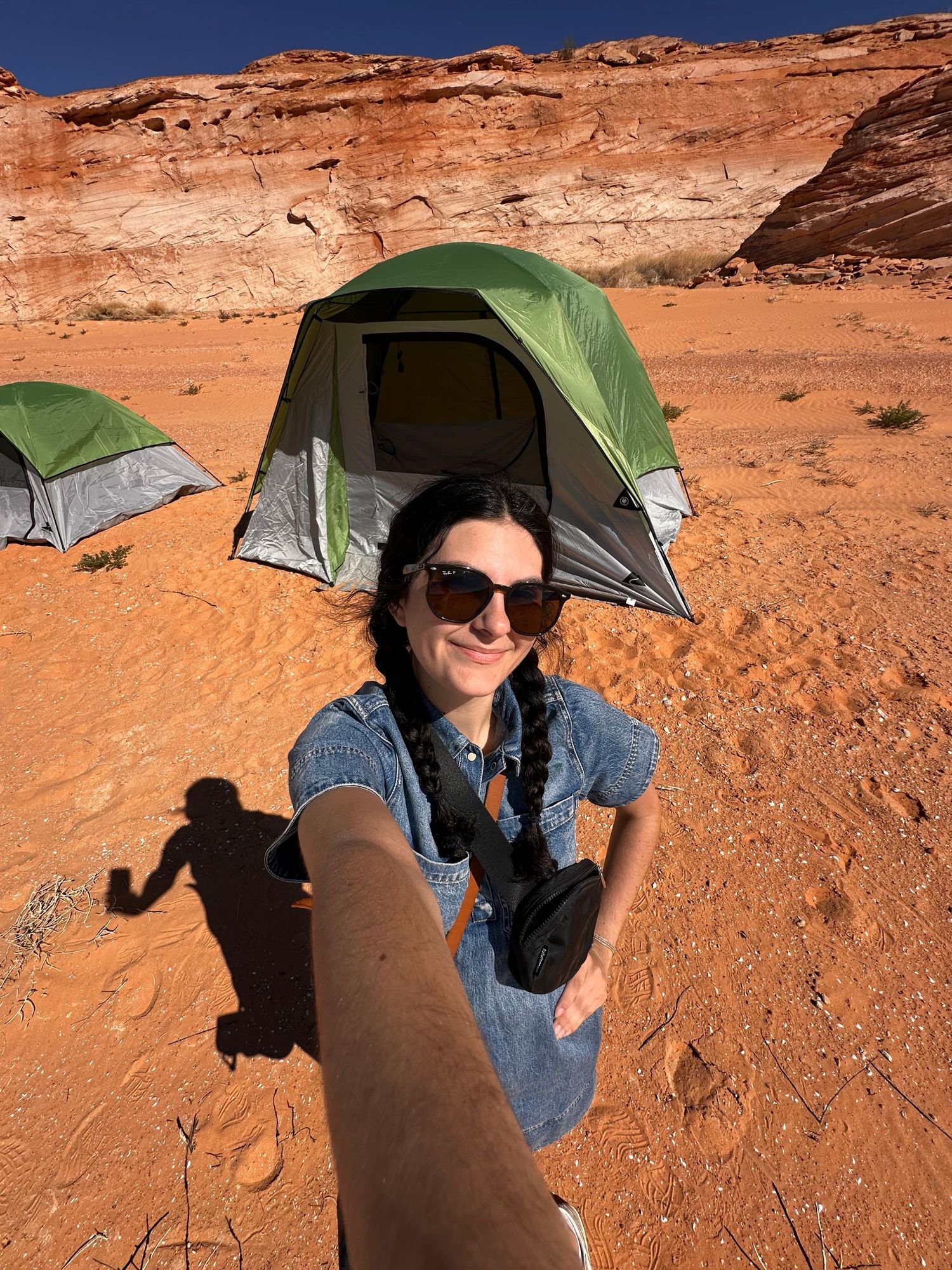 Person taking selfies while sitting in red desert landscape with camping tents.