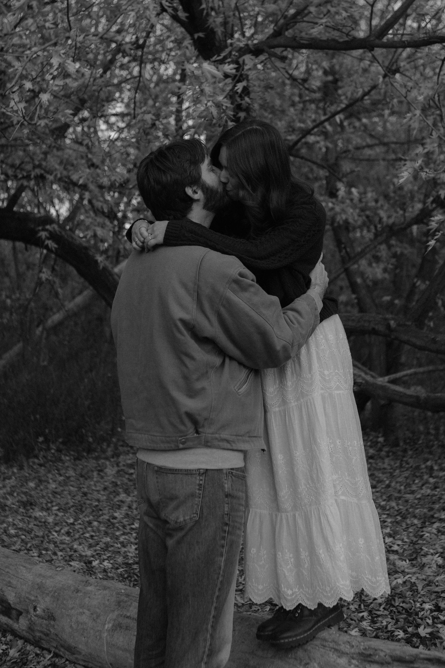 Black and white photo showing couple's tender moment among autumn trees.