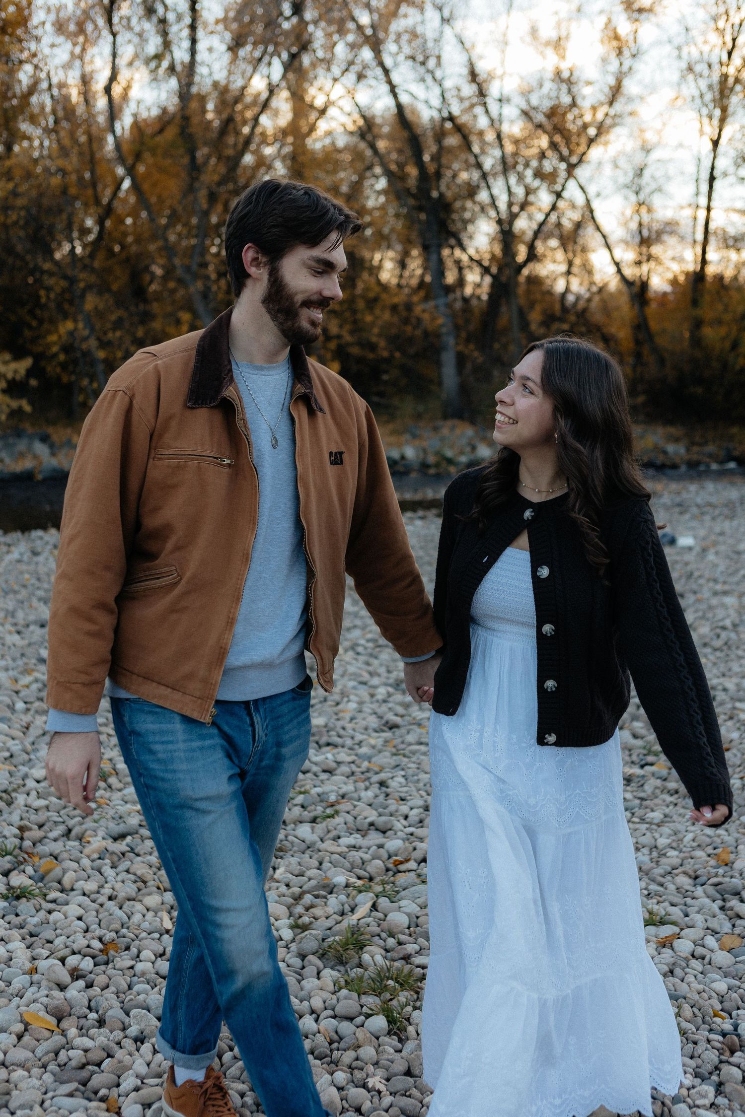 Couple walking together on rocky terrain during autumn with trees in background.