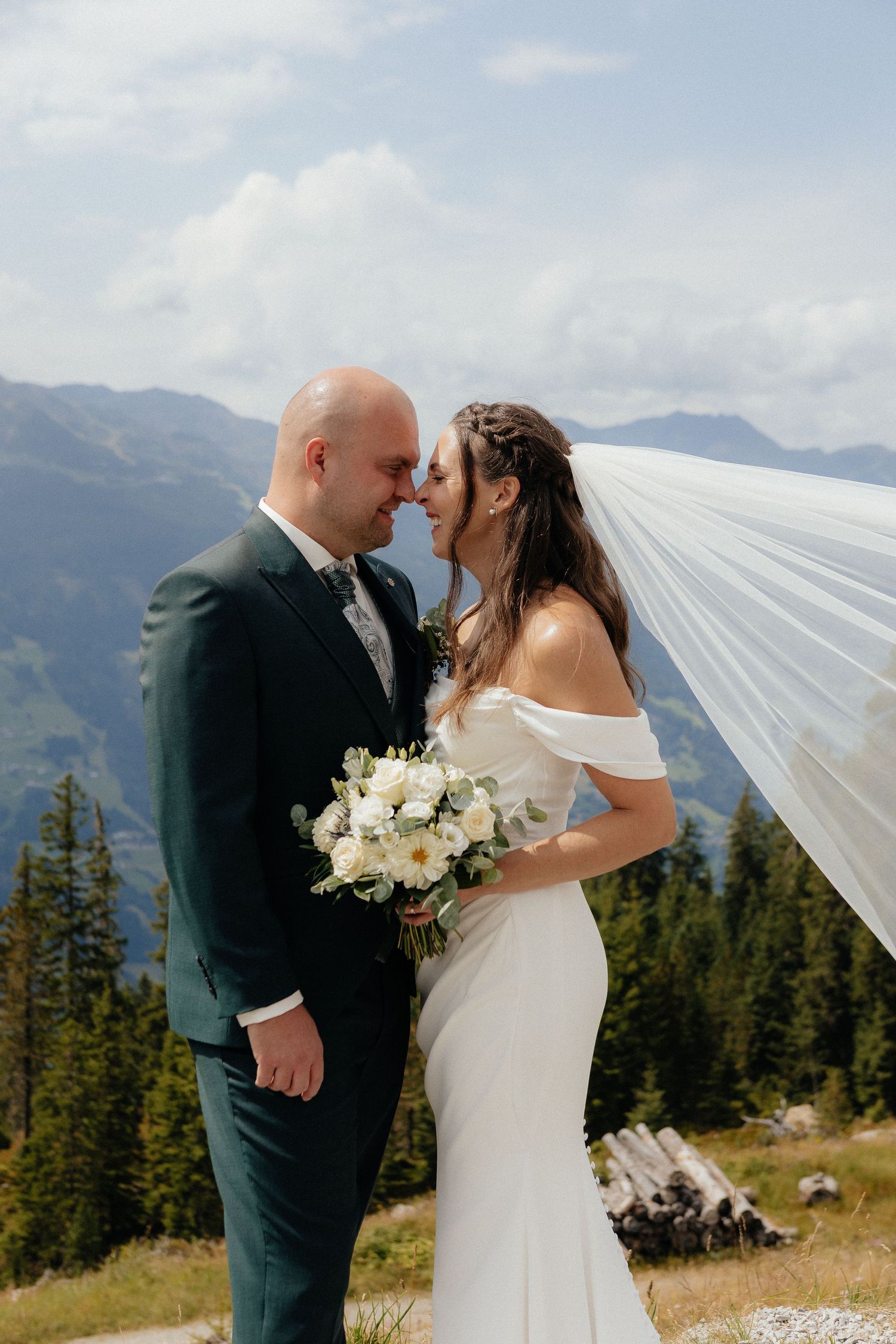 A romantic mountain wedding ceremony with a couple sharing a kiss against a backdrop of evergreen trees and peaks.